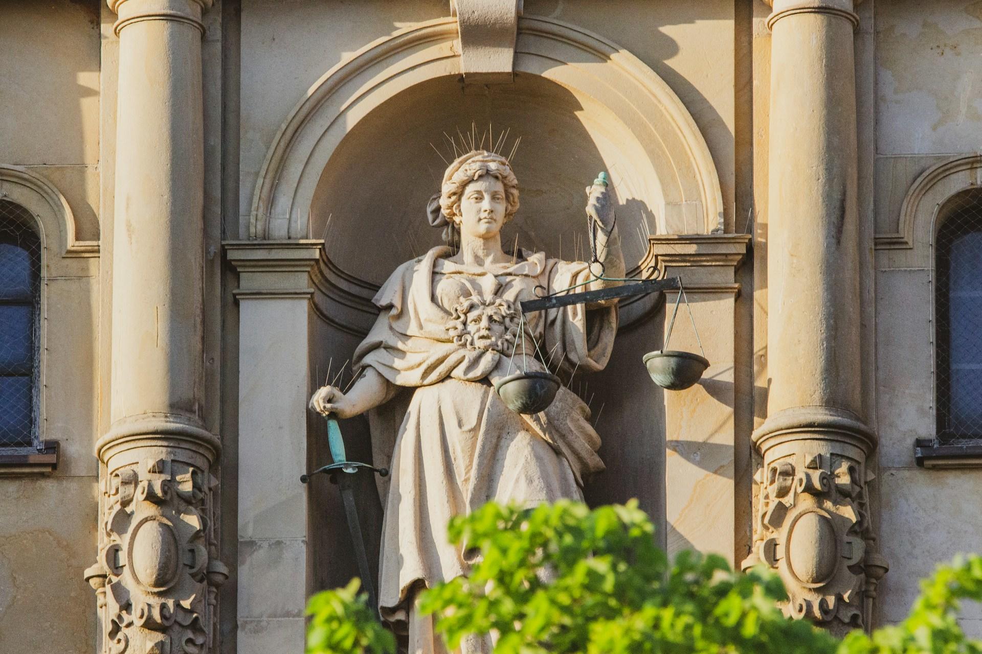 Steinfigur der Justitia in Hamburg solltest du kennen hier in Nahaufnahme mit grünen Büschen davor.