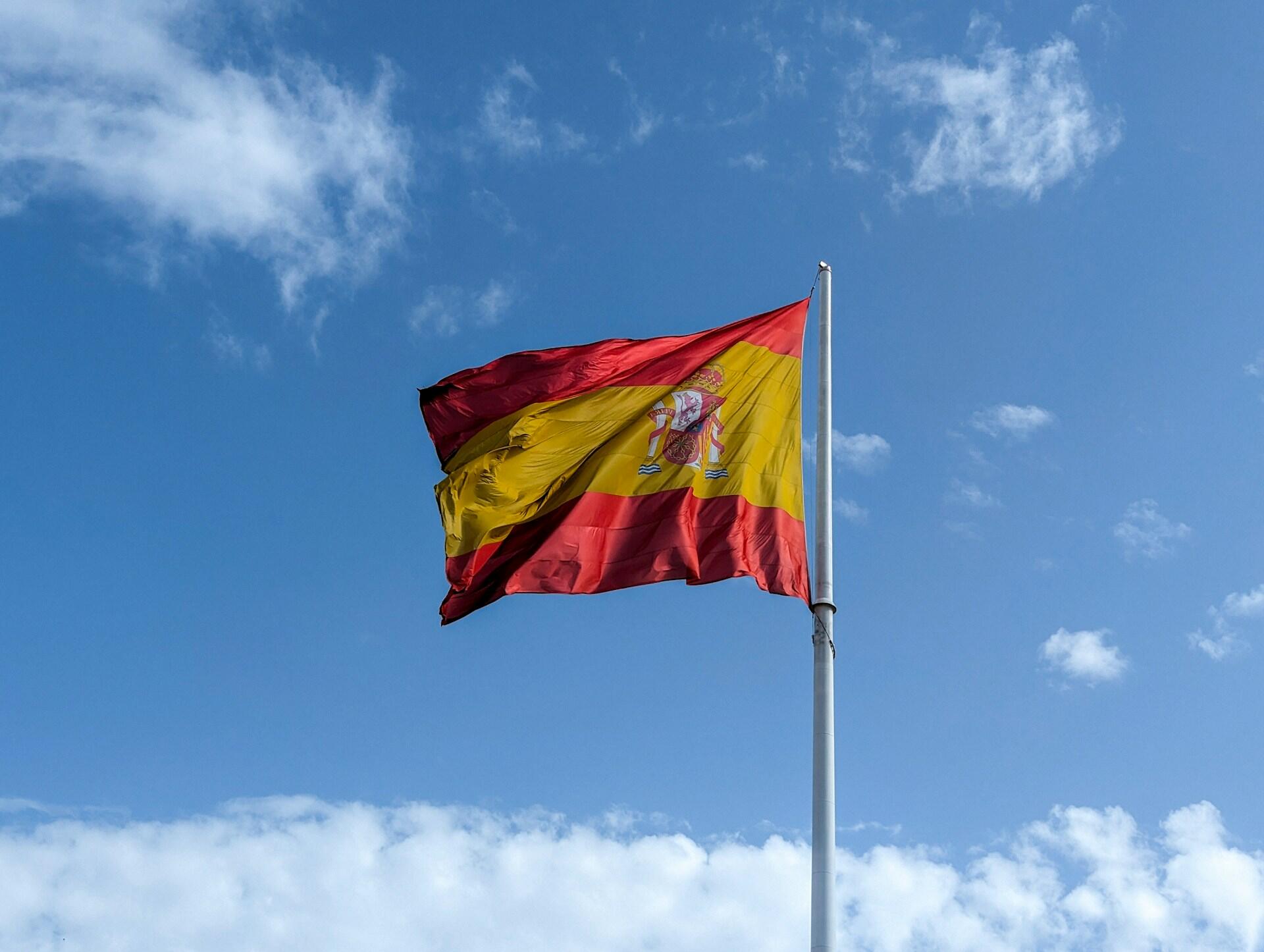 Flagge von Spanien an Mast vor blauem Himmel.