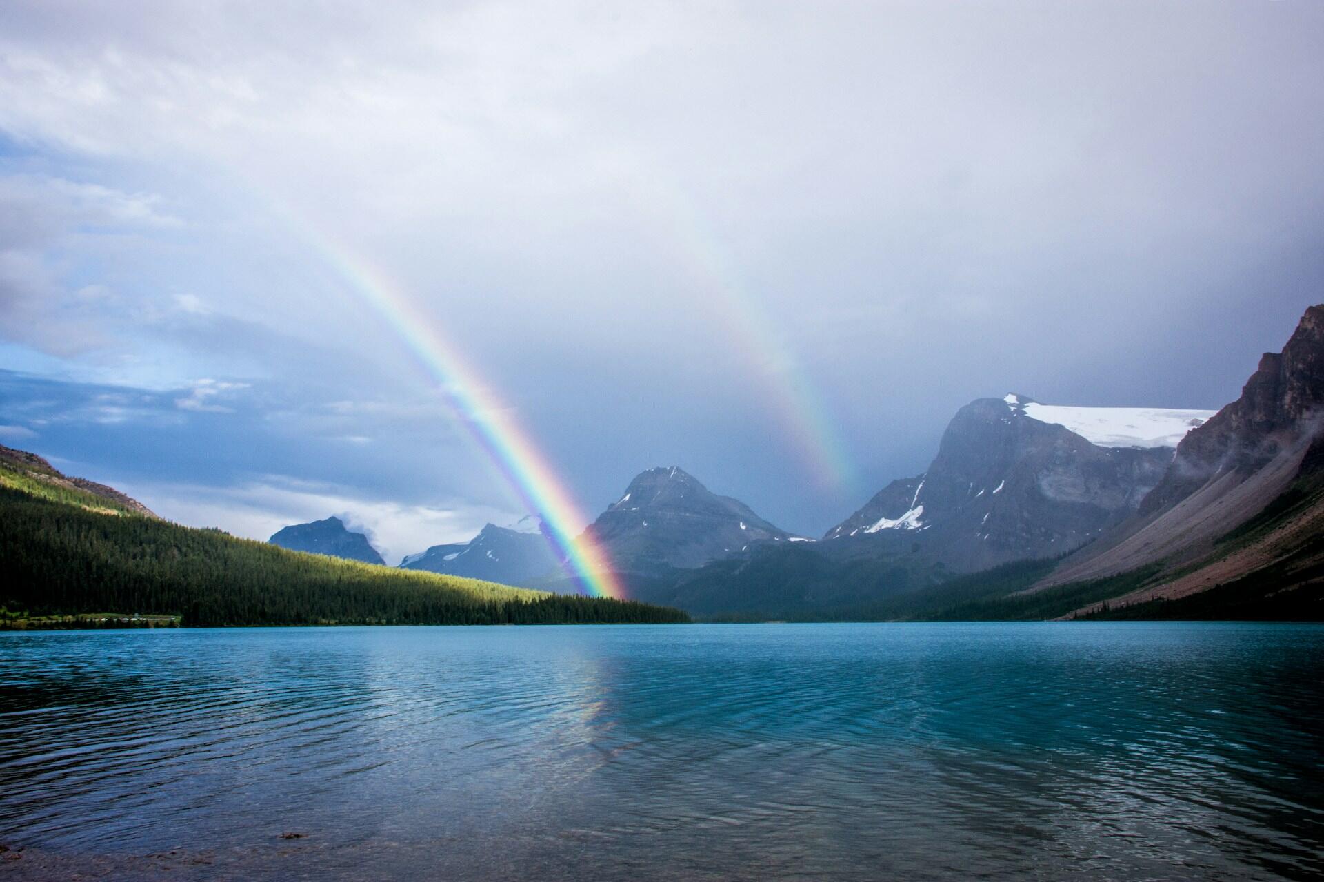 Regenbogen über See vor Gebirge.