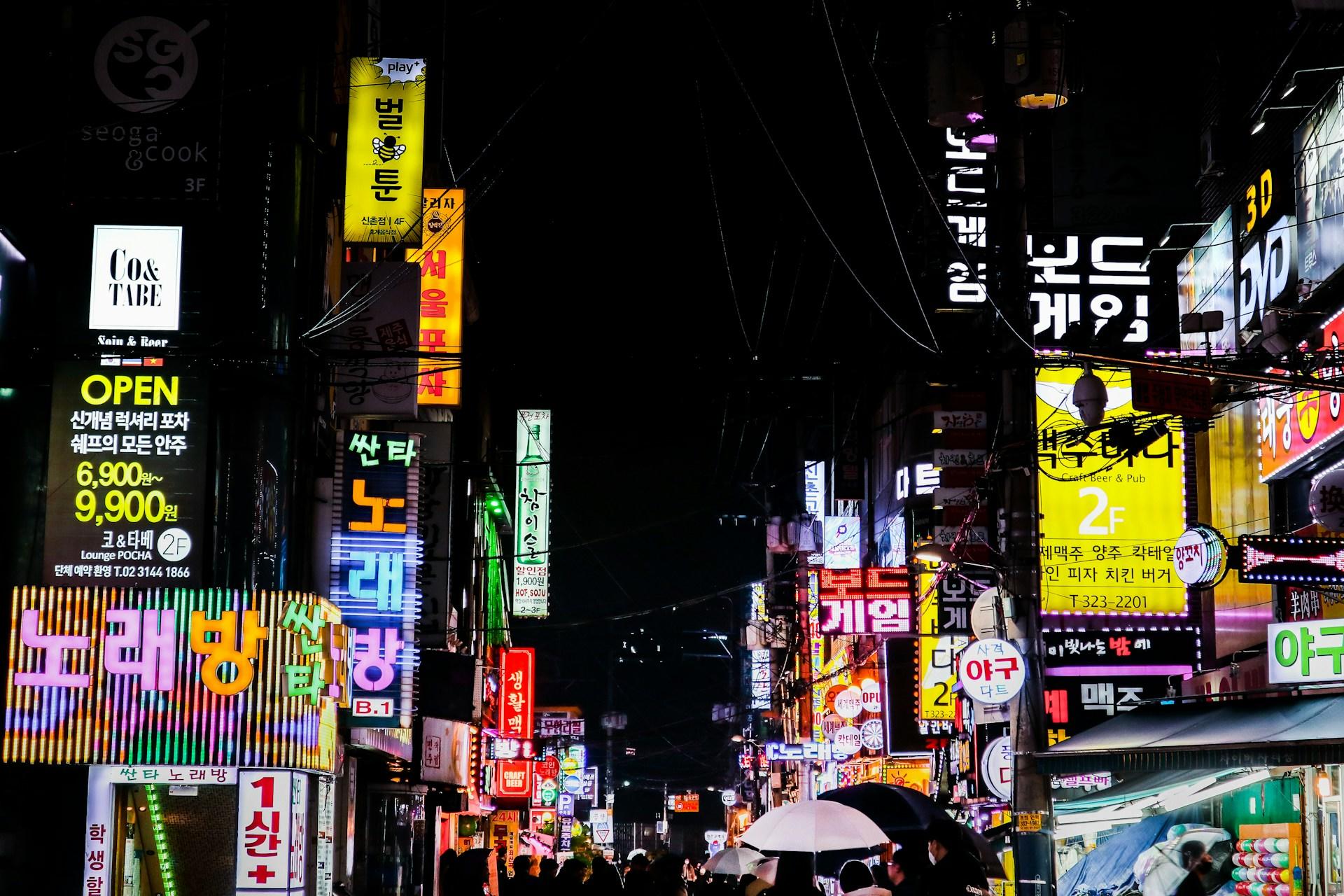 Menschen auf einer Straße zwischen hohen Häusern mit koreanischen Leuchtschriften