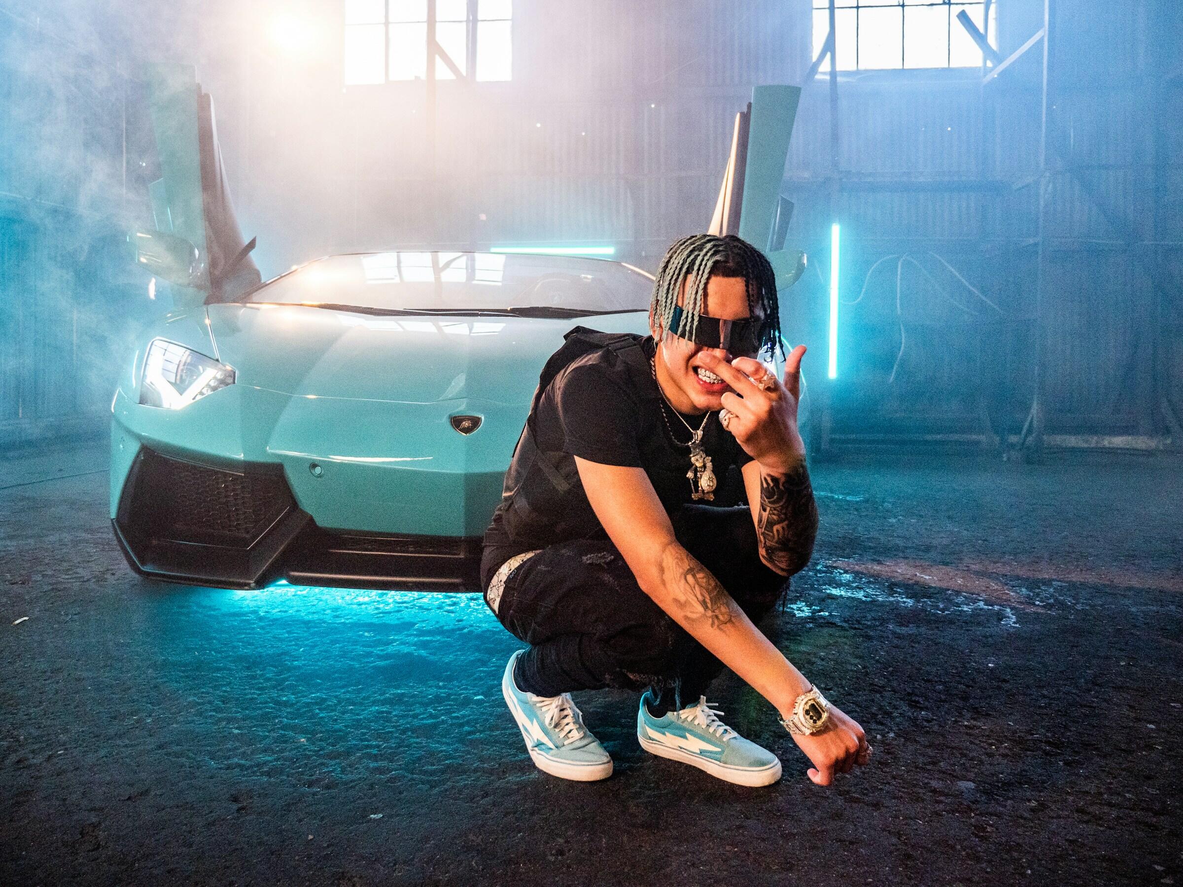 Ein Rapper kniet vor seinem Lambo.