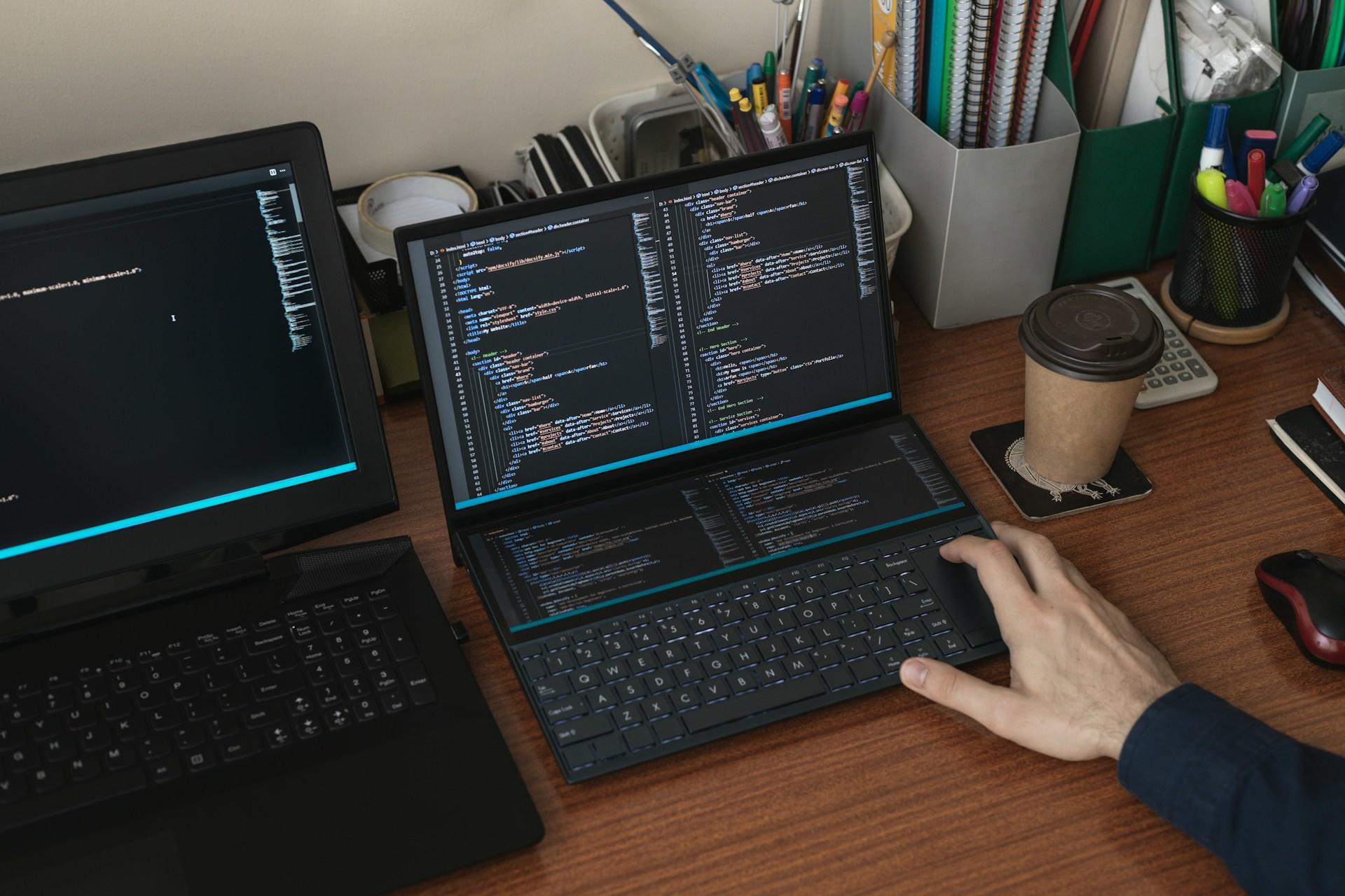 Eine Hand liegt auf einer Tastatur und auf dem Bildschirm ist ein Programmiercode