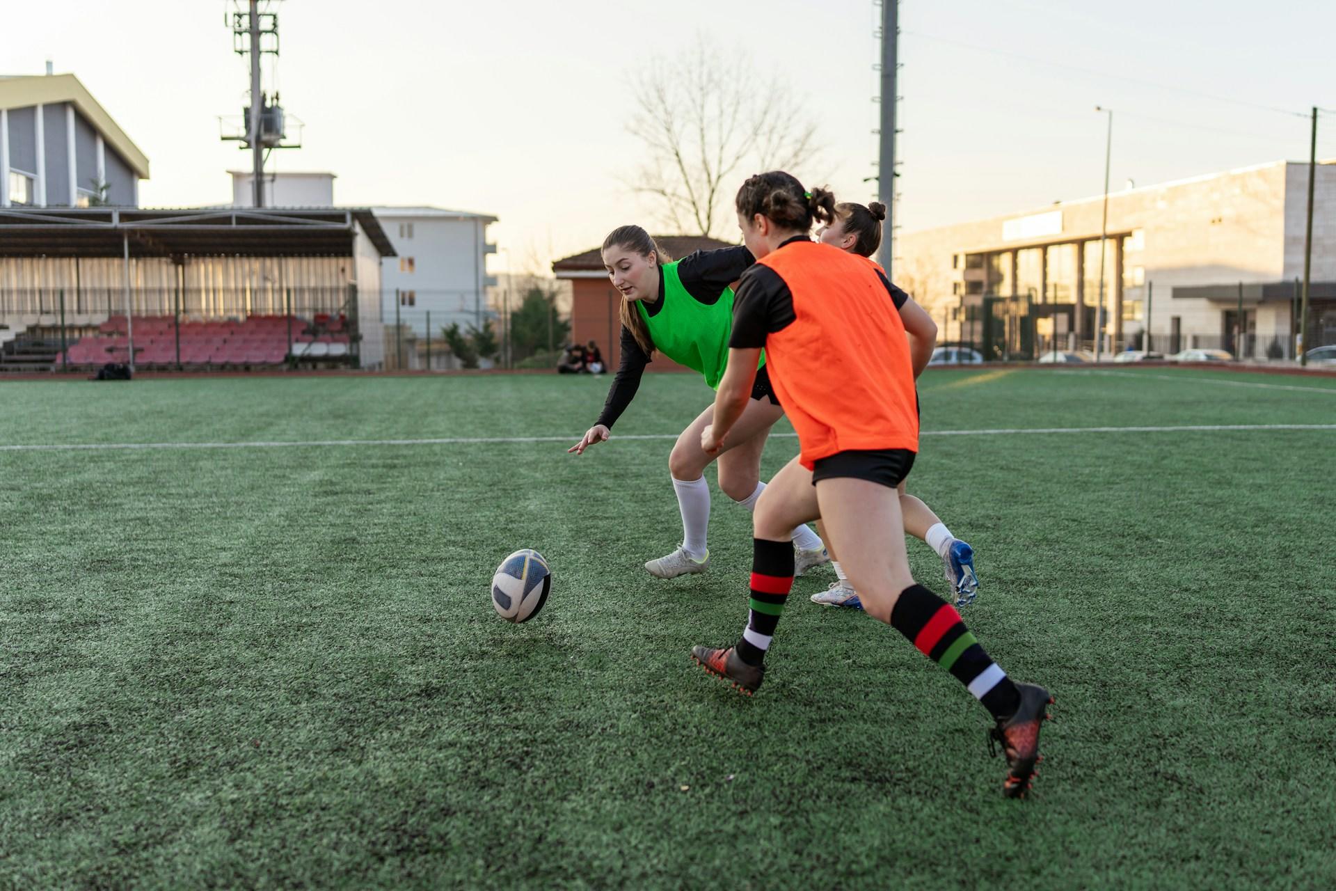 Drei Personen rennen auf einem Fußballfeld auf einen Ball zu