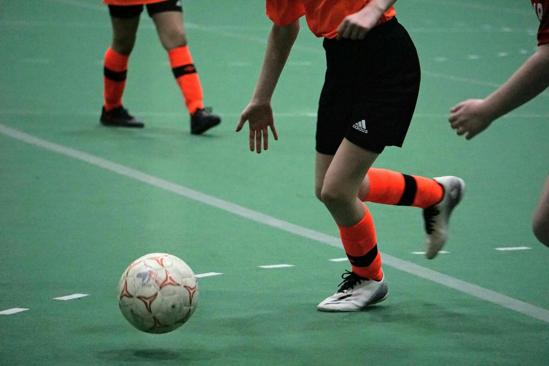 Fussballer mit orangenen Stutzen spielt Ball.