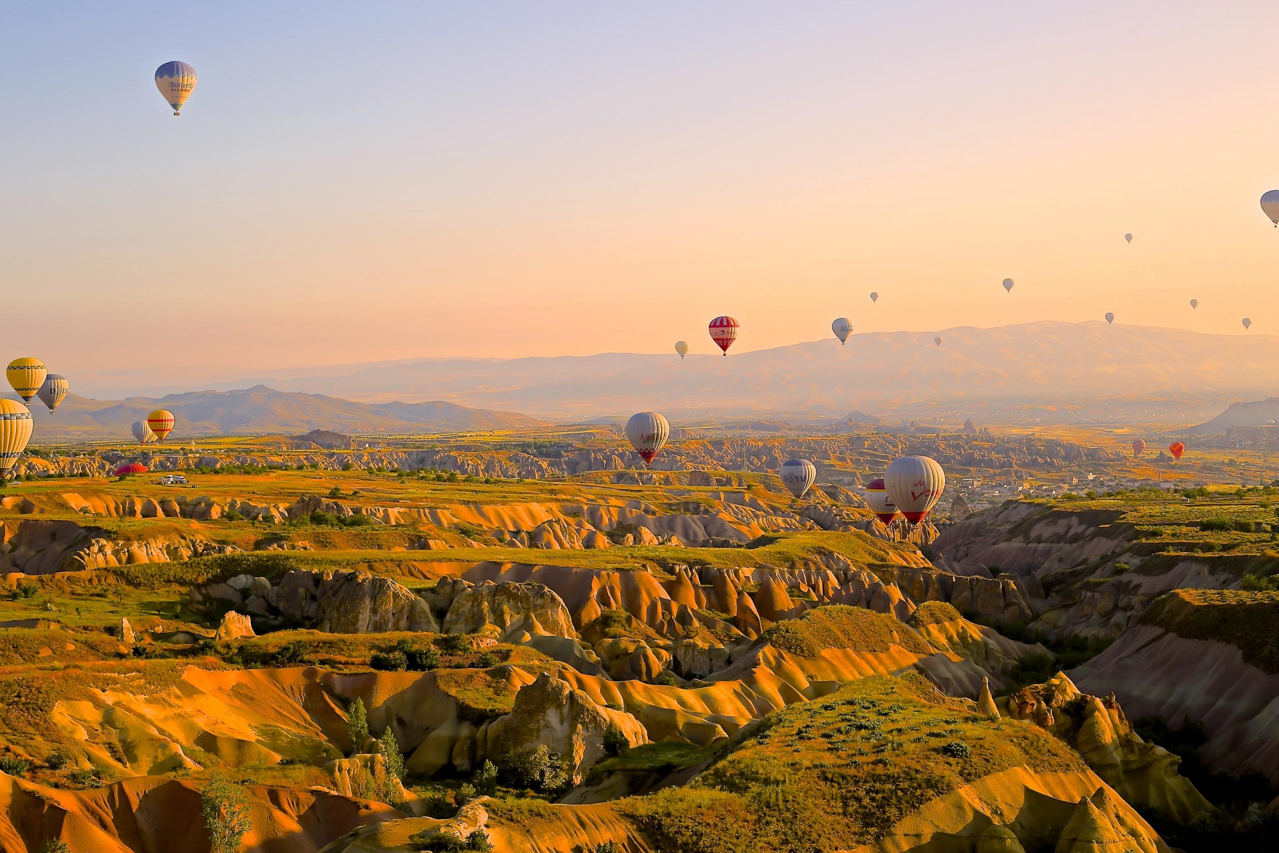 Mehrere Heißluftballons fliegen über bergige Landschaft.