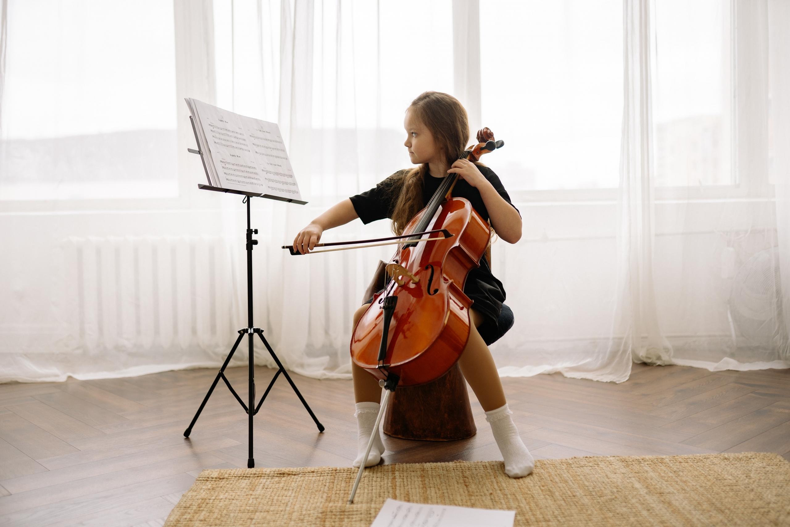 Ein Kind spielt in einem lichtdurchfluteten Raum Cello. Cello lernen ist gut für die Entwicklung von Kindern.