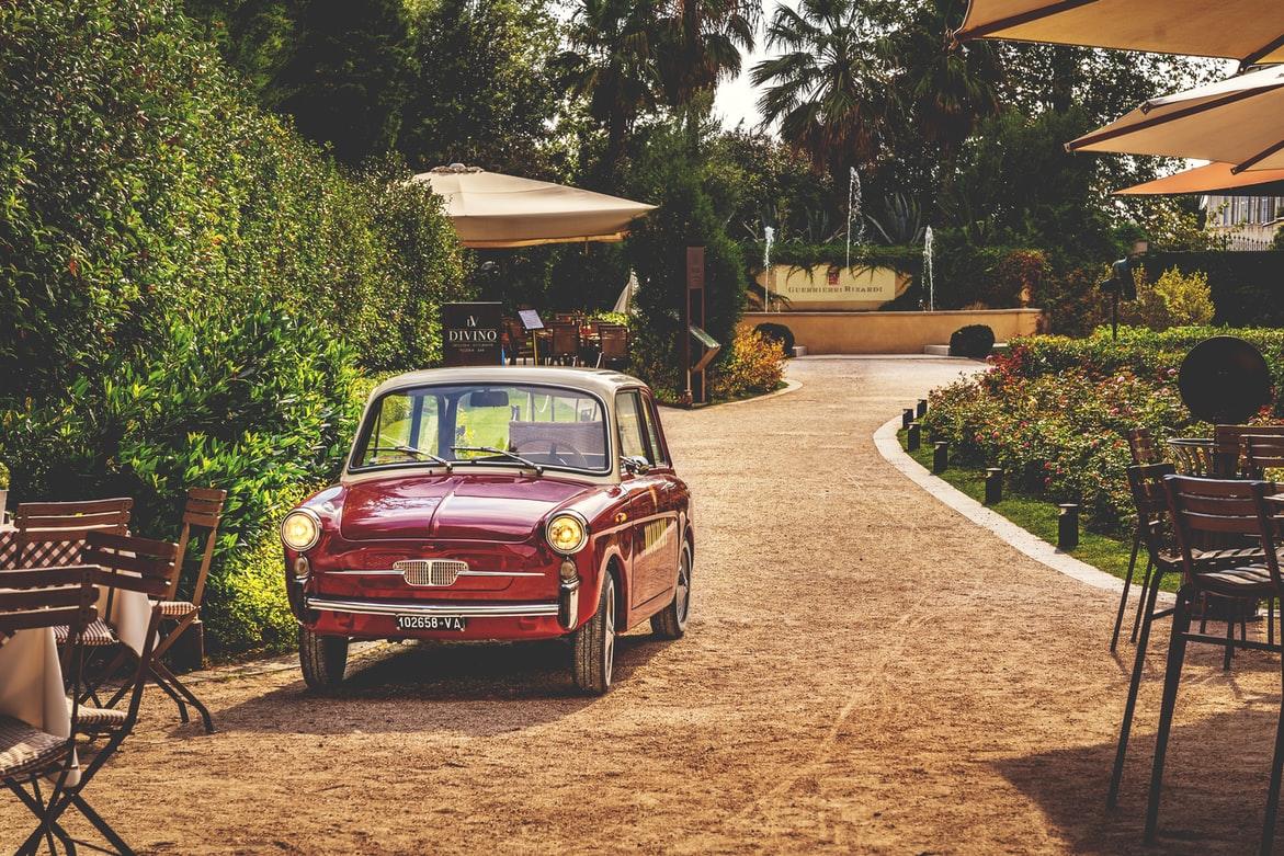 Ein kleines rotes italienisches Auto in einer bepflasterten Einfahrt umgeben von Tischen und Sonnenschirmen. Selbst dieses Bild lockt in den Süden! Italienischkurse in Bremen bereiten Dich perfekt auf Deine Italienreise vor.