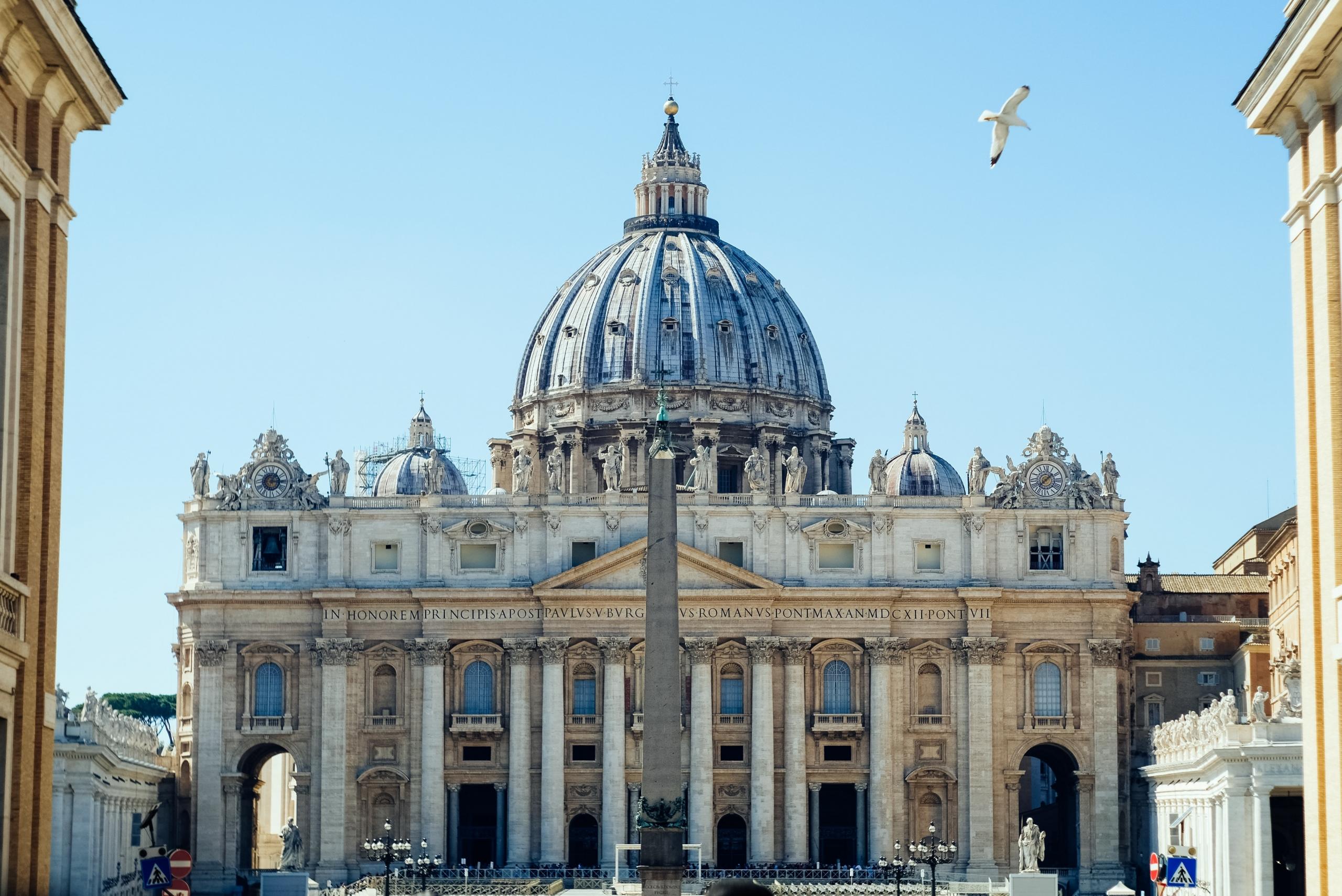 Zwischen zwei Häusern Blick auf den  Petersdom vor blauem Himmel.