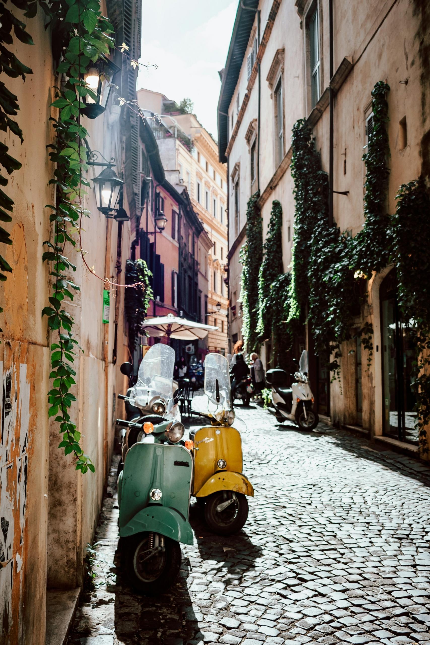 Nicht nur die Museen sind in der italienischen Hauptstadt sehenswert auch kleine Gasse wie diese mit einer geparkten grünen und einer gelben Vespa.