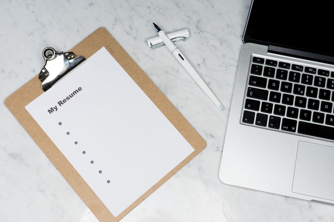 Ein Klippbrett mit einem Blatt Papier, auf dem "My Resume" steht, daneben ein Stift und ein Laptop: Zur erfolgreichen Bewerbung gehören auch gute Unterlagen - auch das lernst Du in der Berufsberatung.
