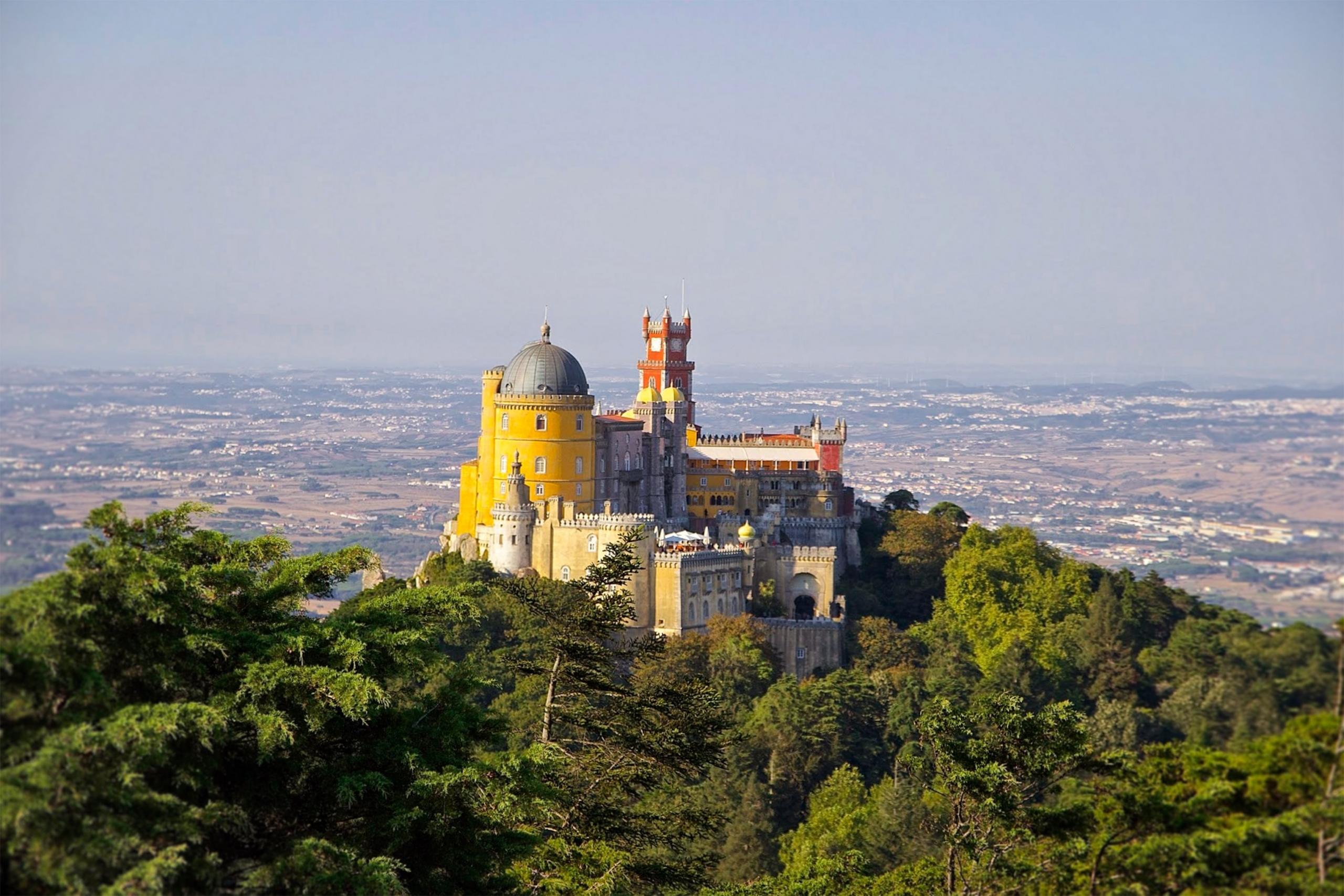 Der Nationalpalast Pena ragt in bunten Farben auf einem Hügel über die Landschaft. Er gehört zu den wichtigsten Denkmälern Portugals.