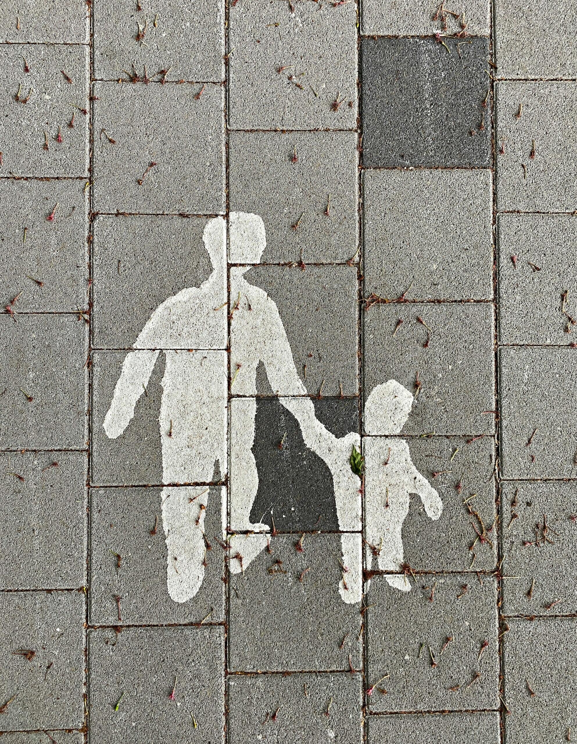 EIne Straßenbemalung mit einem Elternteil, dass das Kind an die Hand nimmt.