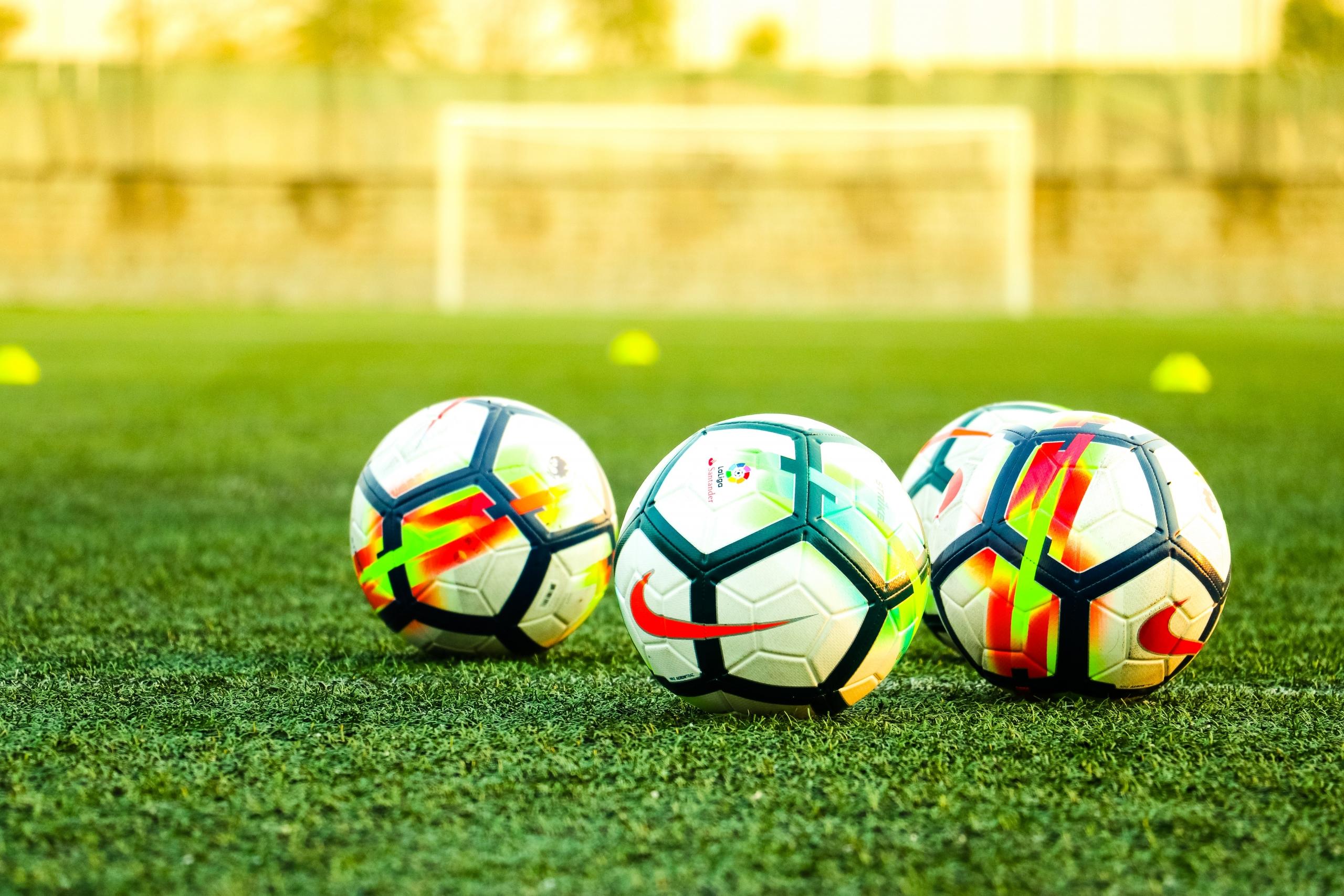 Drei Fußbälle liegen auf einem Rasenfeld. Im Fußballtraining kann man nie genug Bälle haben.