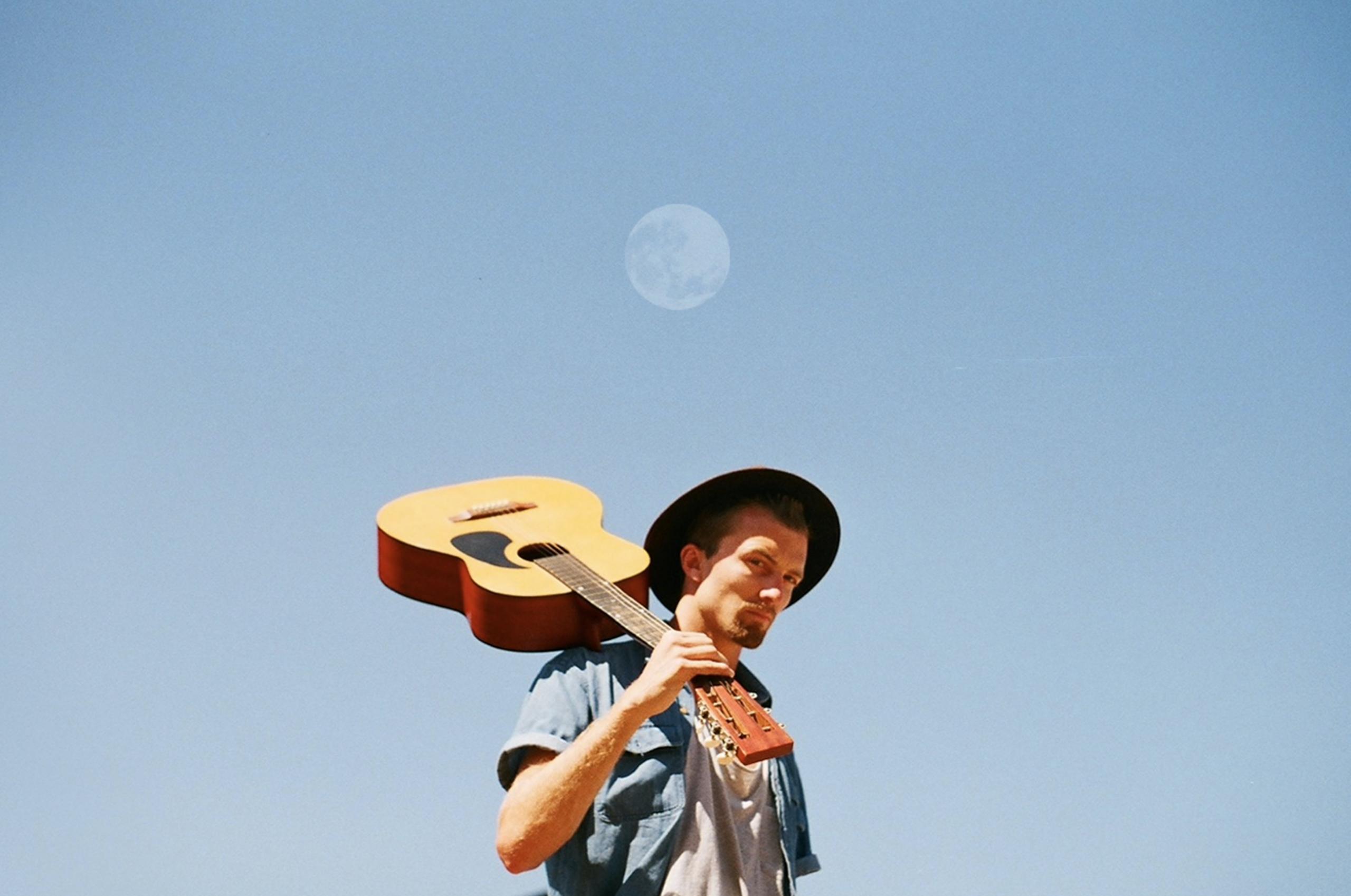 Die Gitarrre lässig auf der Schulter tragend, posiert der Gitarrist unter dem Mond.