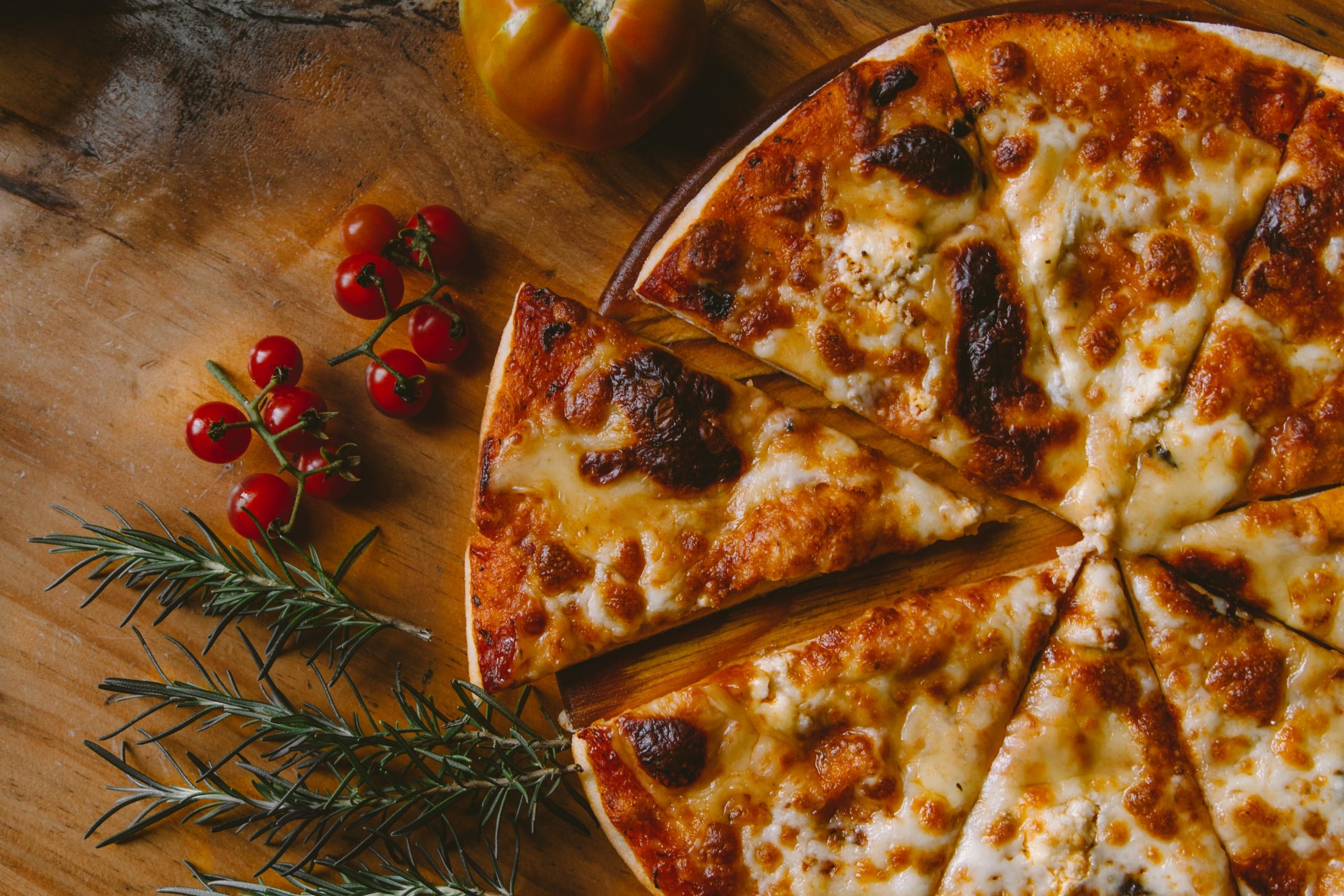 Pizza Margherita auf einem Holztisch; dekoriert mit roten Johannisbeeren und Rosmarin. Auch Pizza lässt sich glutenfrei zubereiten.