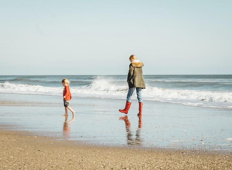 Mutter und Tochter spazieren am Strand. Die Mutter ist da, aber das Kind ist frei.