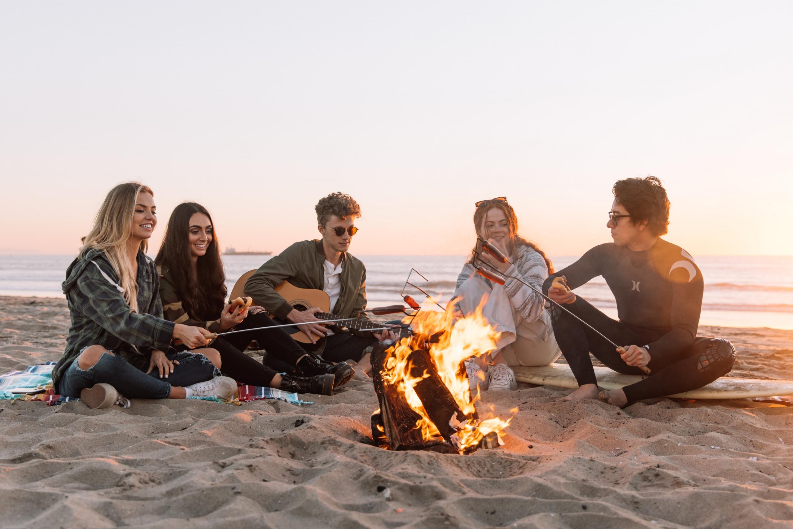 Ein Lagerfeuer am Strand, umringt von Freunden, ist der beste Ort, um auf der Gitarre ein paar Songs zu spielen.