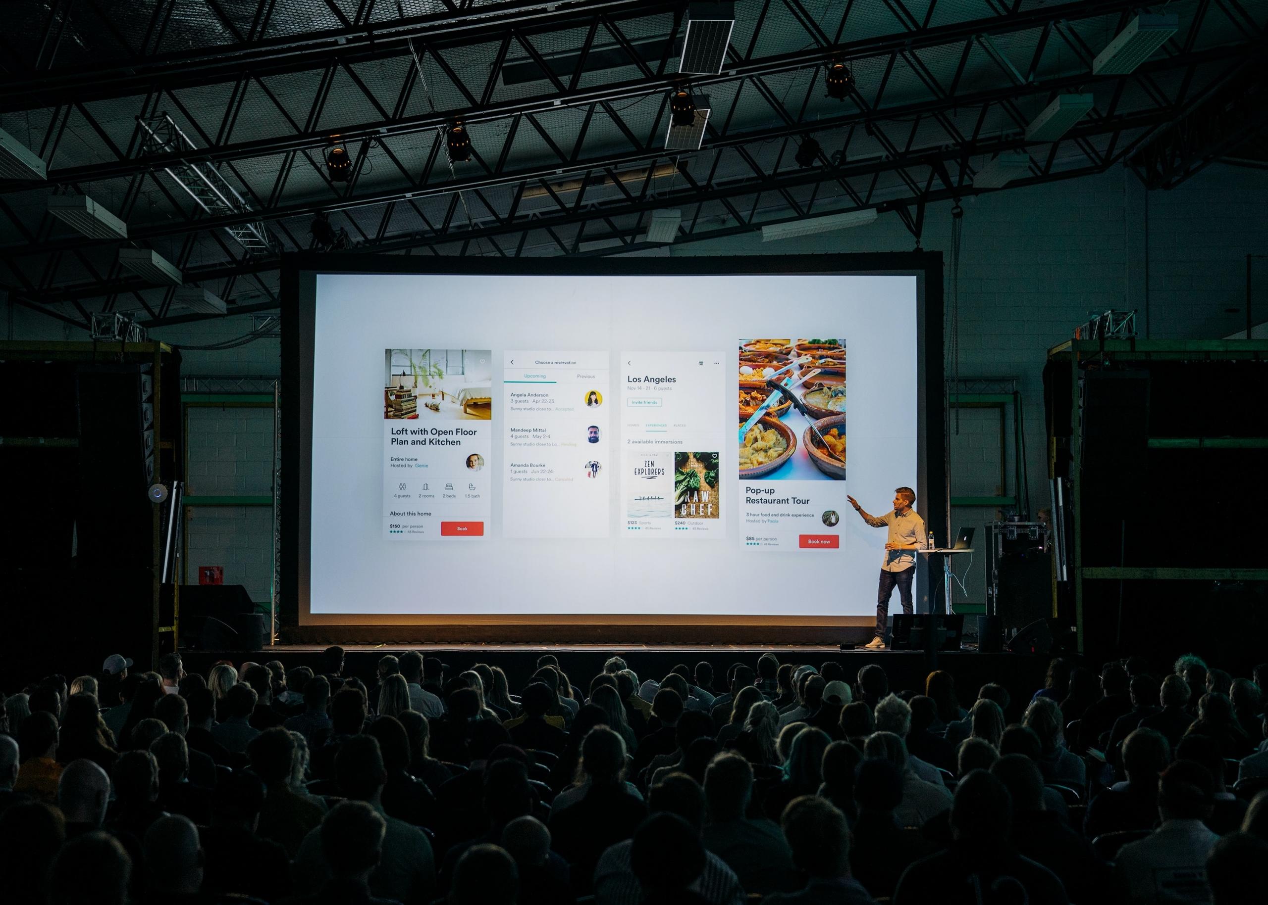 Eine Person präsentiert an einem großen Bildschirm vor vielen Menschen. Möchtest auch du mit PowerPoint präsentieren?