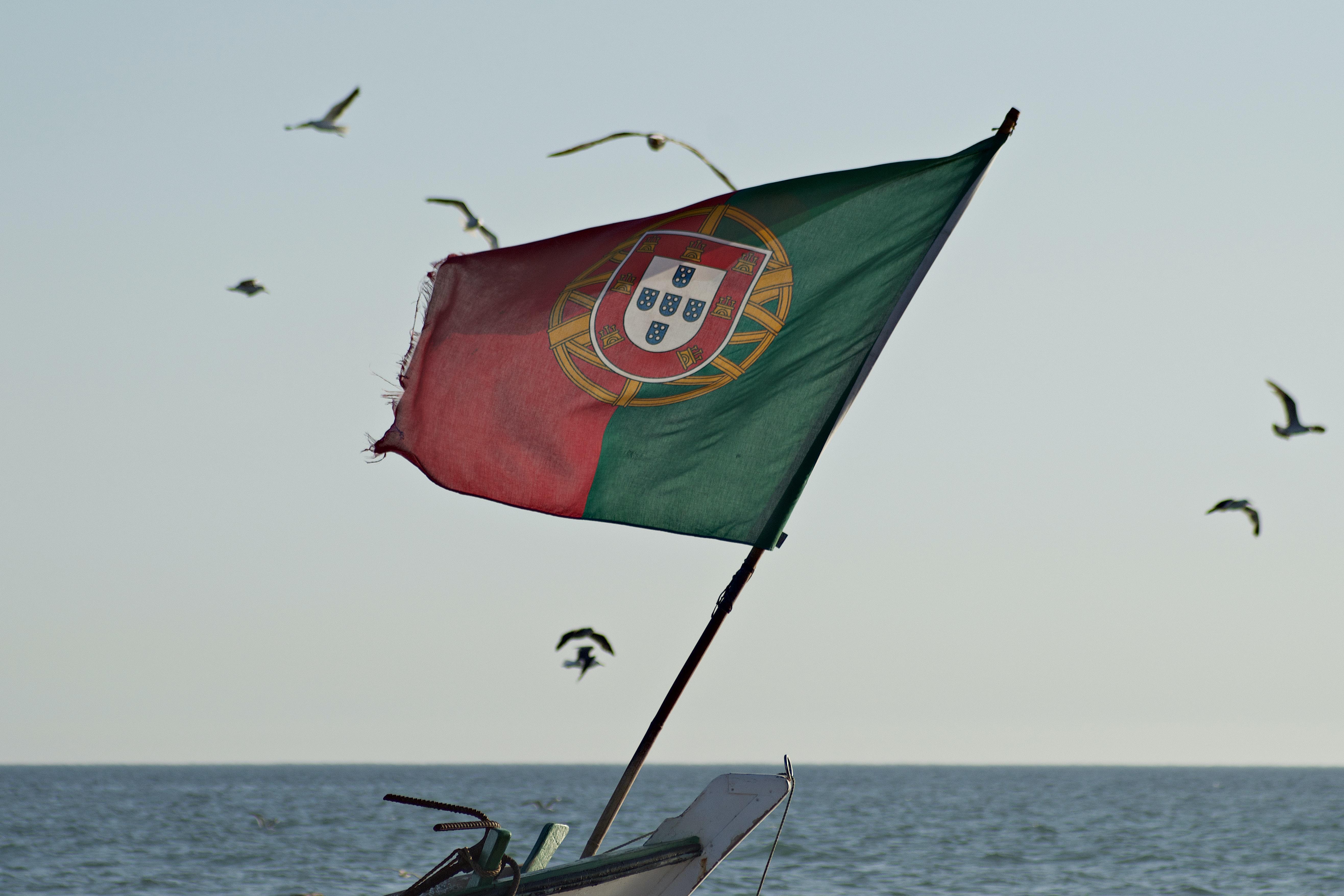 Die Flagge Portugals weht über dem Meer. Die Kosten für den Portugalurlaub können stark variieren.