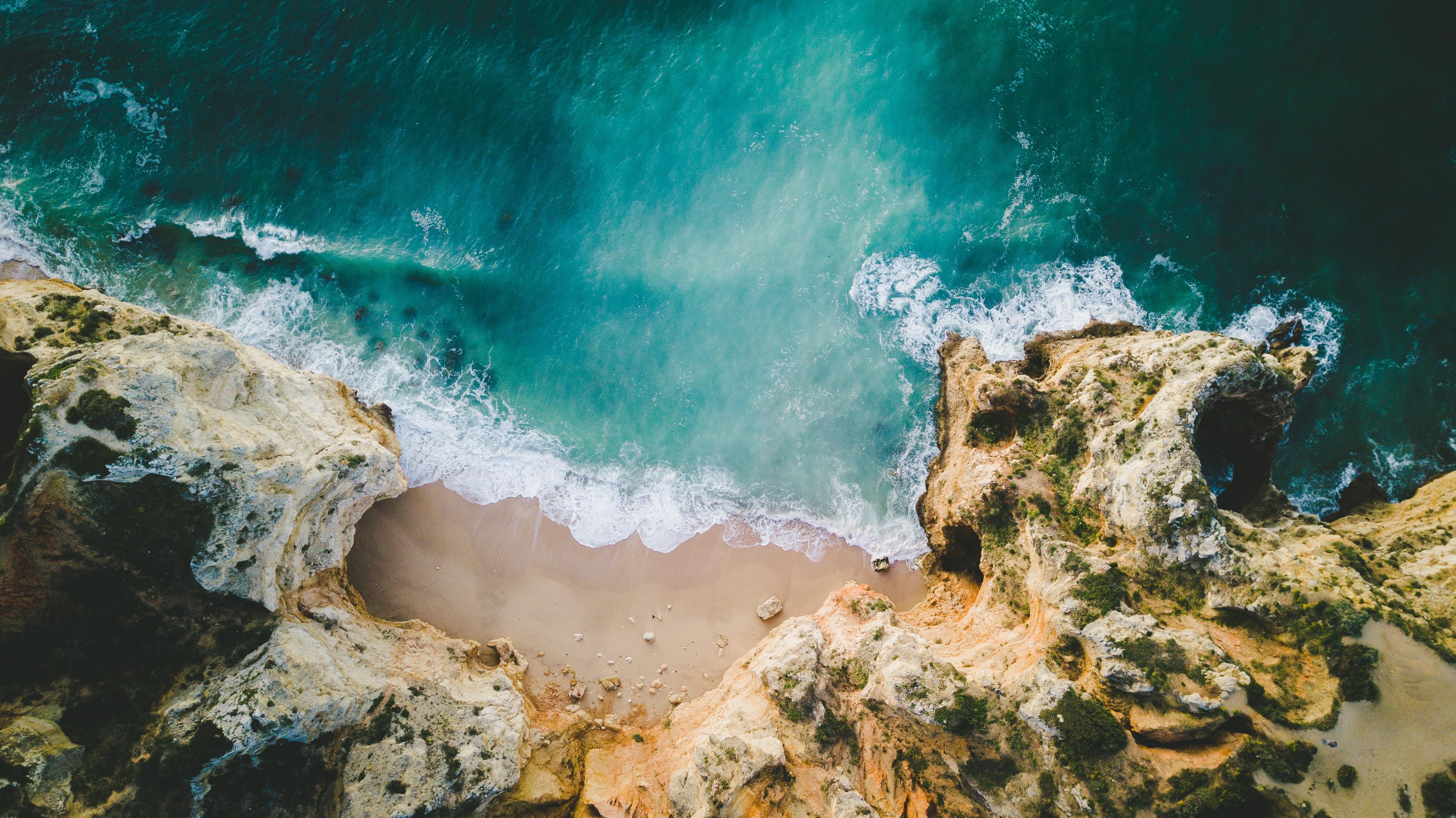 Wellen treffen auf eine von Felsen umgebene Sandbucht. Solche Umgebungen findet ihr beim Urlaub in Portugal zuhauf!