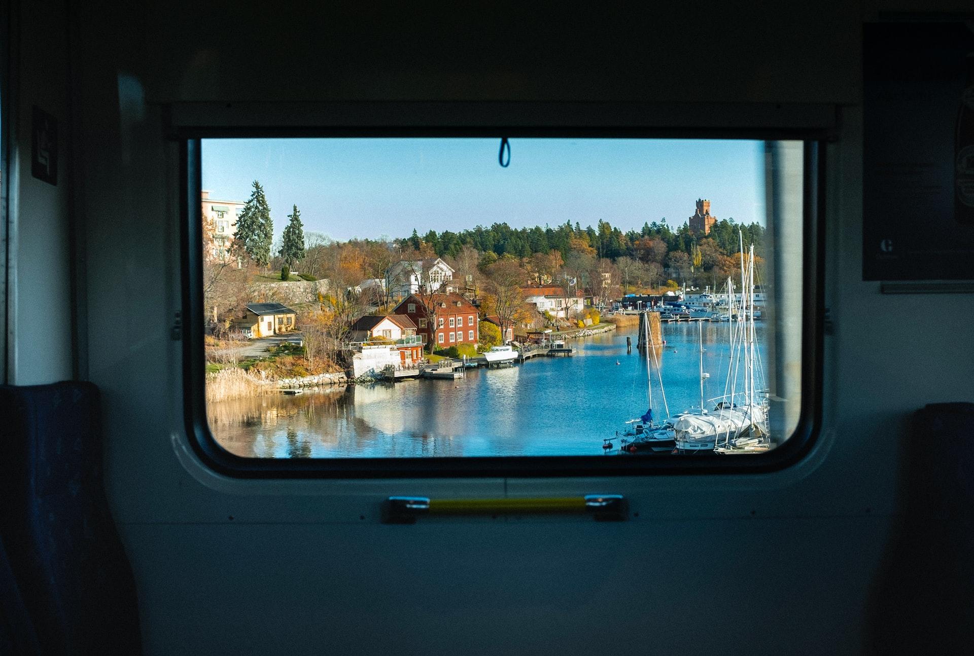 Durch ein Zugfenster sieht man ein schwedisches Dorf am Wasser unter blauem Himmel. Informationen über Jobs im Land finden!