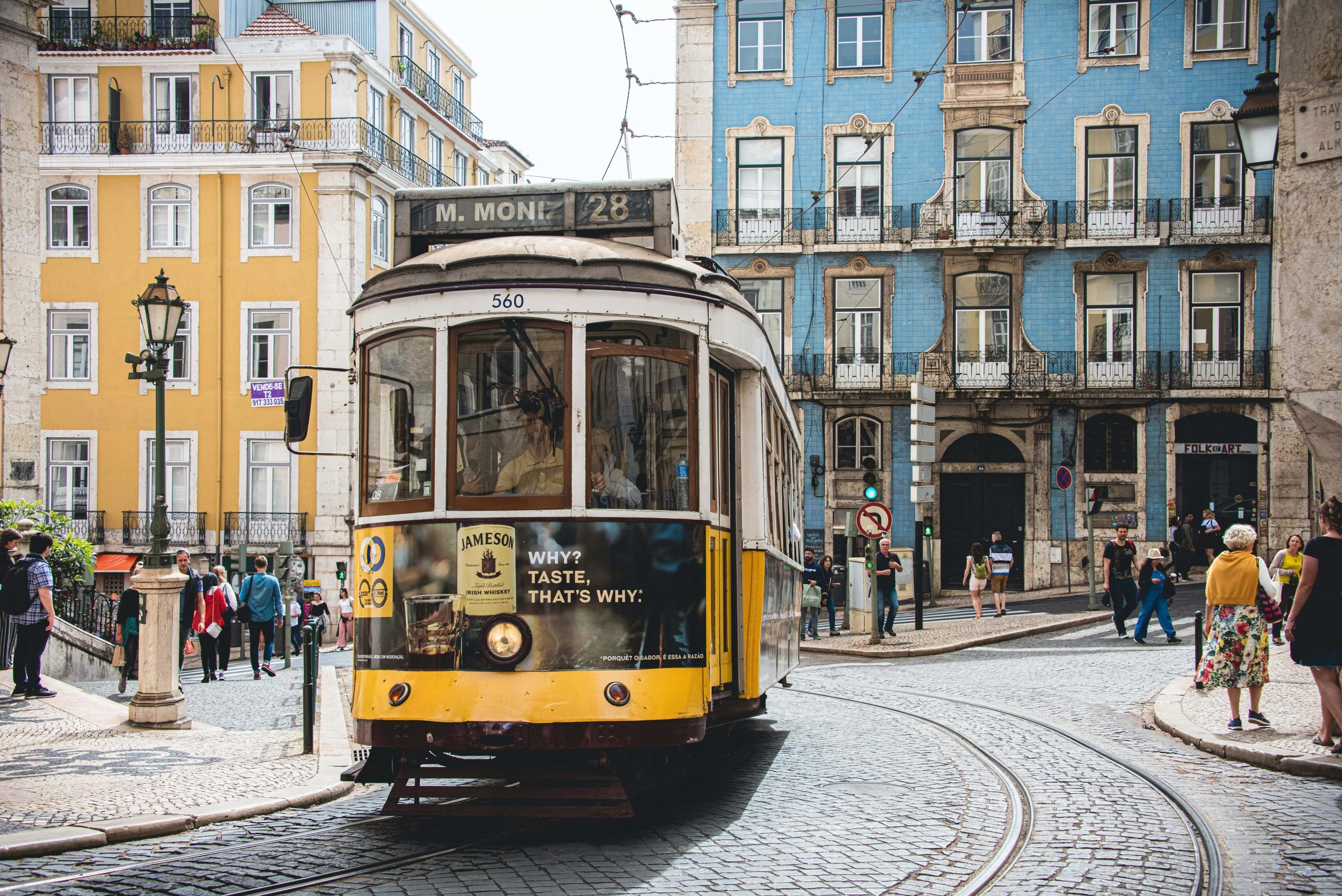 Eine traditionelle gelbe Straßenbahn fährt durch das Zentrum von Lissabon. Diese Art von Transport erhöht zwar im Vergleich zur U-Bahn das Budget für euren Urlaub in Portugal, macht aber umso mehr Spaß.