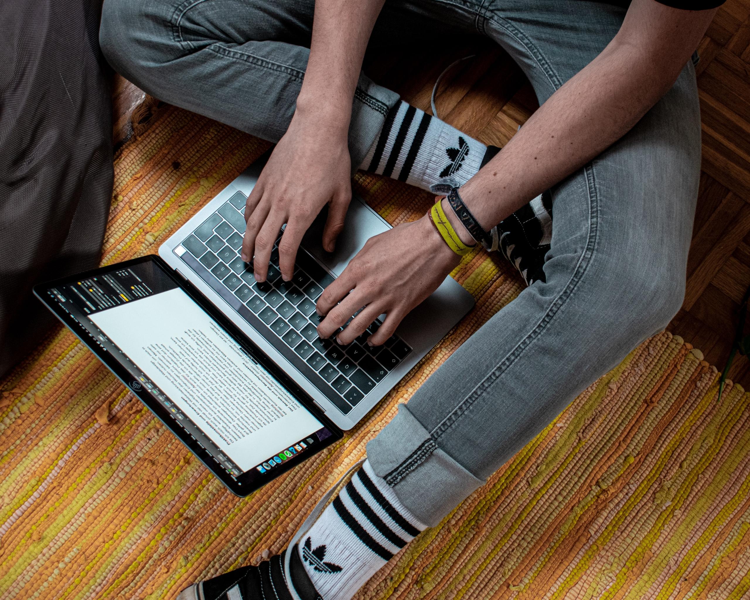 Ein Mann sitzt auf dem Boden und arbeitet am Computer. Willst auch die die Funktionen von Word erlernen?