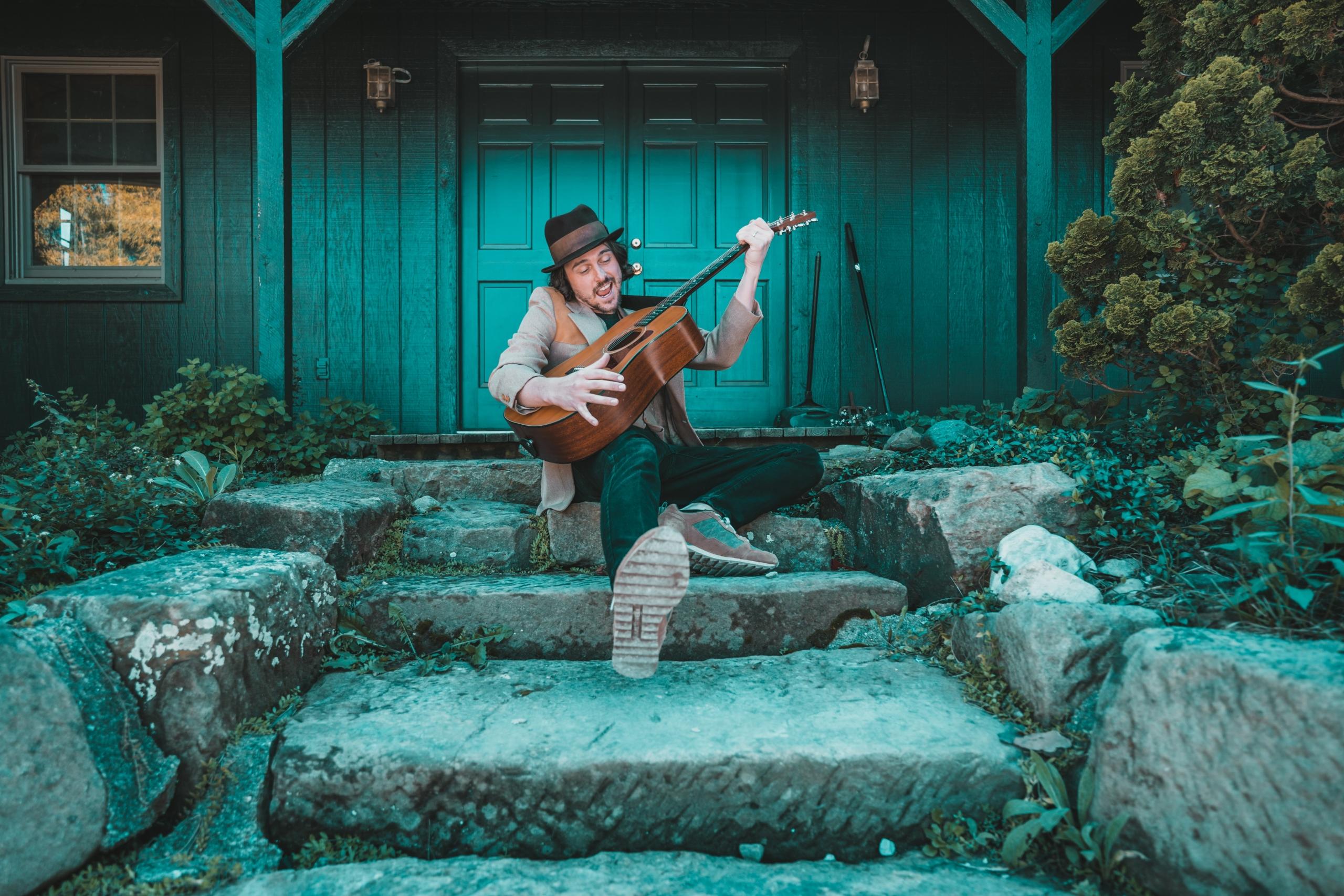 Ein Mann sitzt auf einer Treppe und hat richtig viel Spaß beim Gitarre spielen.