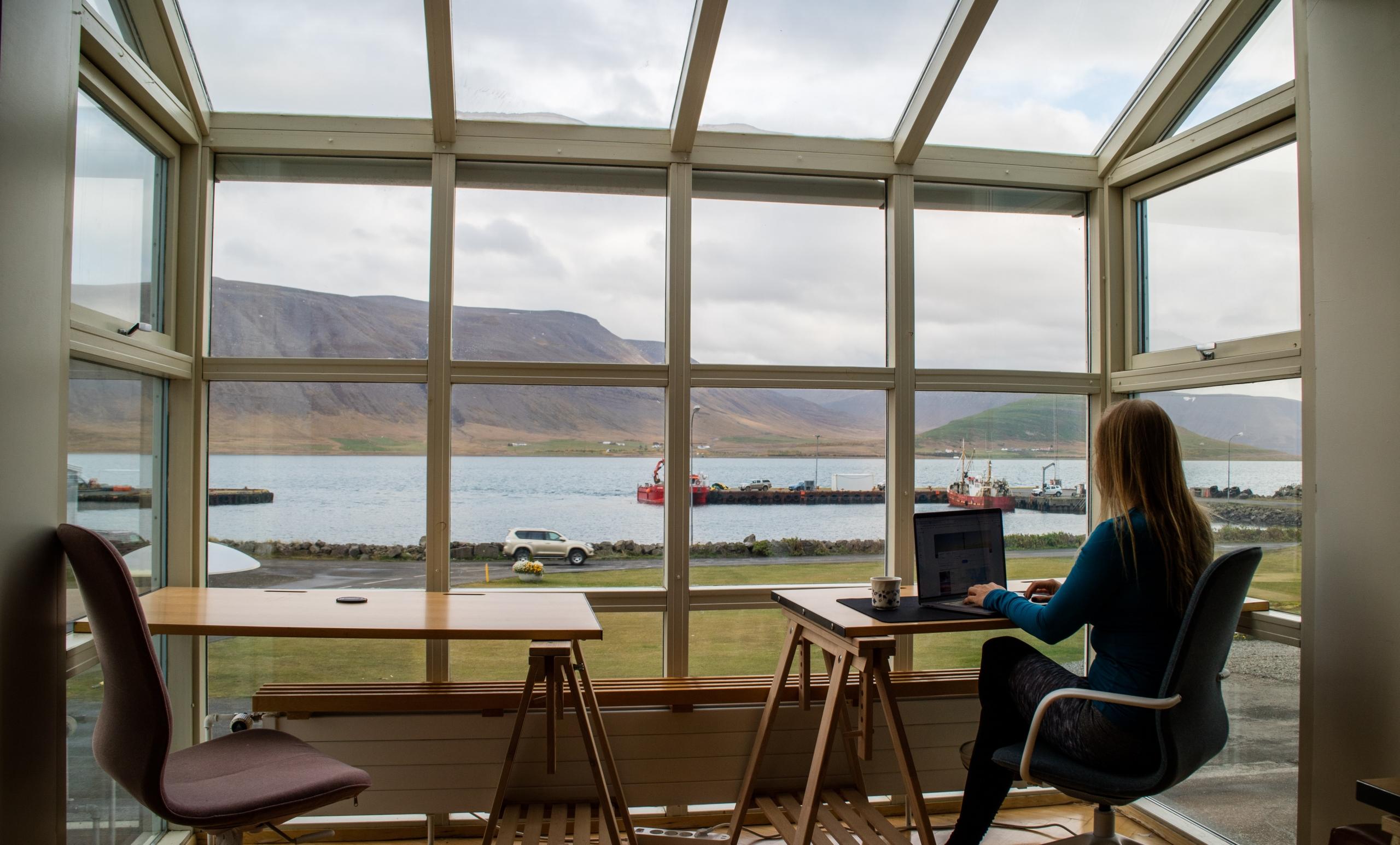Eine Frau sitzt am Computer in einem Café mit Ausblick. Willst auch du lernen, Texte am Computer zu schreiben mit Word? Wir erklären: Was ist Word?