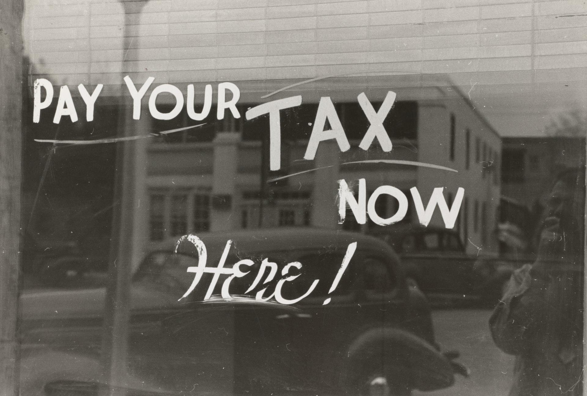 Schwarz-Weiß-Foto einer Aufschrift auf einem Fenster mit den Worten: "Pay your tax here now".