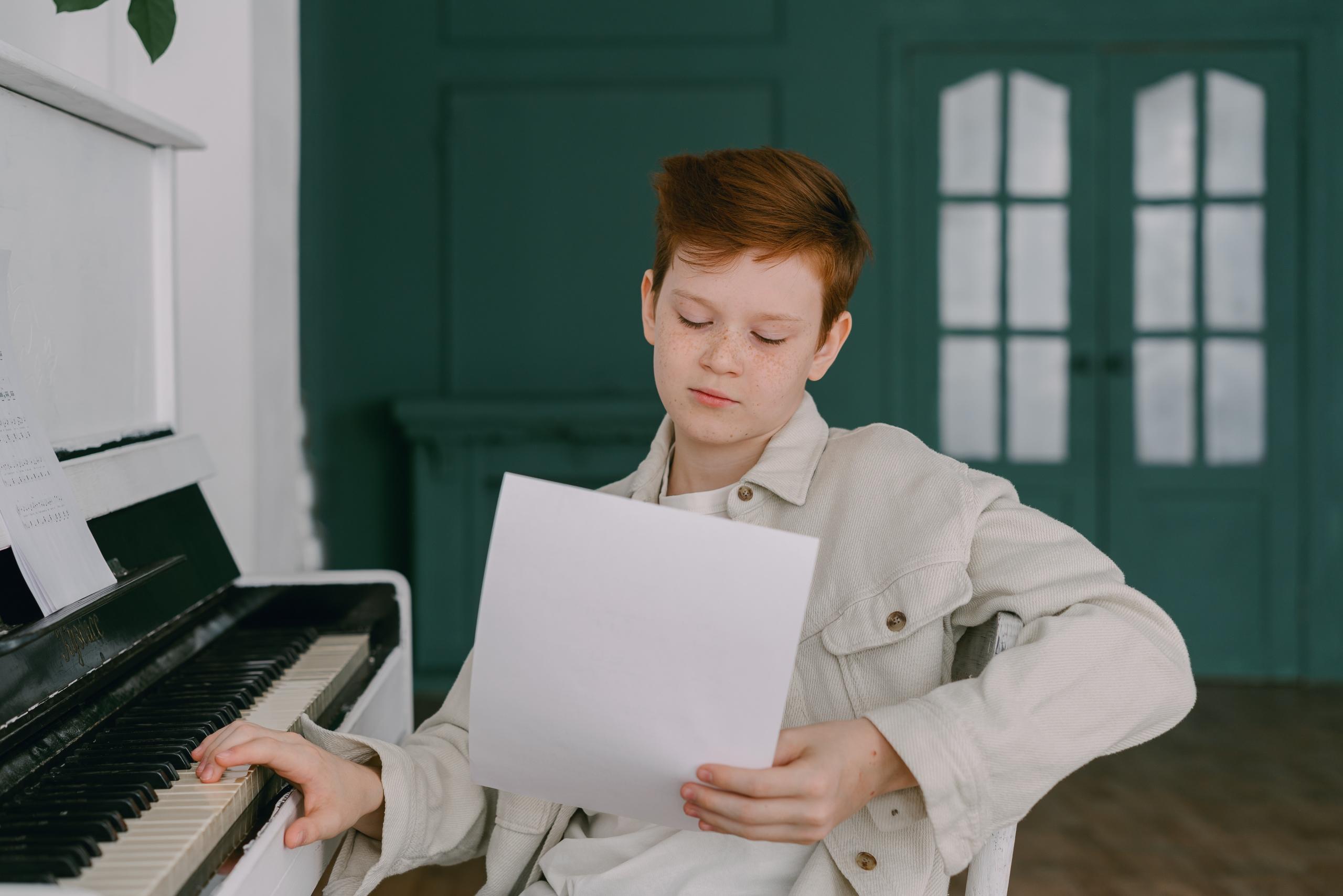 Dieser Junge studiert konzentriert das Notenblatt, bevor er anfängt, das Lied auf dem Klavier zu spielen.
