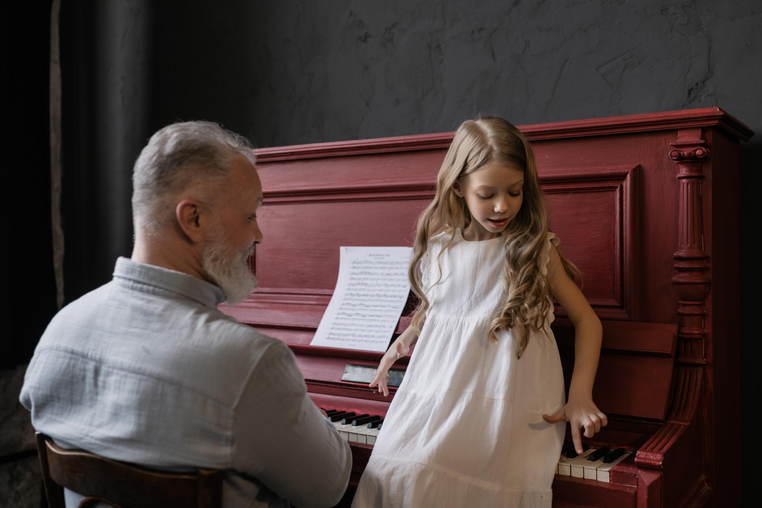 Ein älterer Herr und ein Mädchen sitzen gemeinsam am Klavier. Gemeinsames Musizieren kann von der ersten Stunde Klavierunterricht an gepflegt werden.