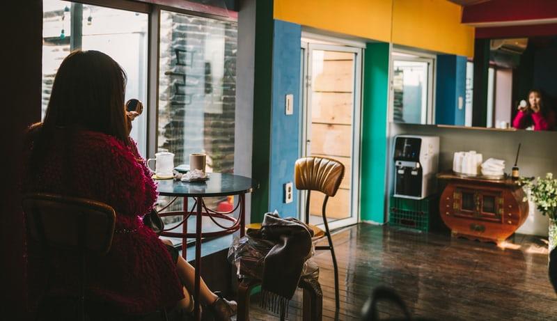 Der bunte Eingangsbereich eines Hostels in Seoul, auf einemStuhl an einem kleinen Tisch trinkt eine Frau einen Kaffee.