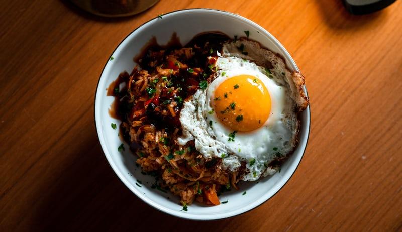 Auf einem Holztisch steht eine Schale mit Bibimbap, einem koreanischen Reisgericht.