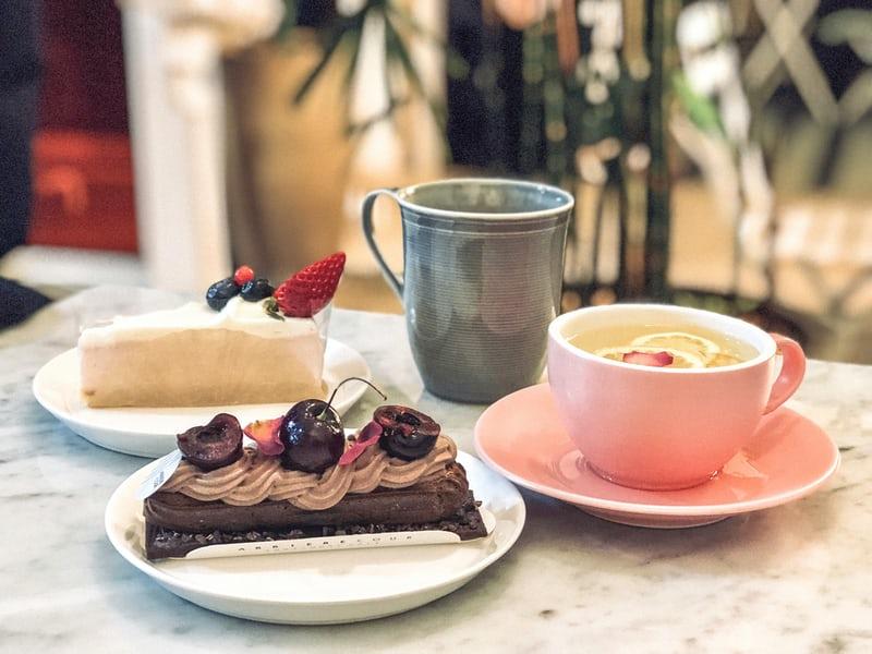 Ein gedeckter koreanischer Kaffetisch mit Kaffee in einer rosa Tasse, Tee in einem grauen Steingut-Becher und zwei verschiedene Sorten appetitlicher Kuchen auf zwei Tellern. 