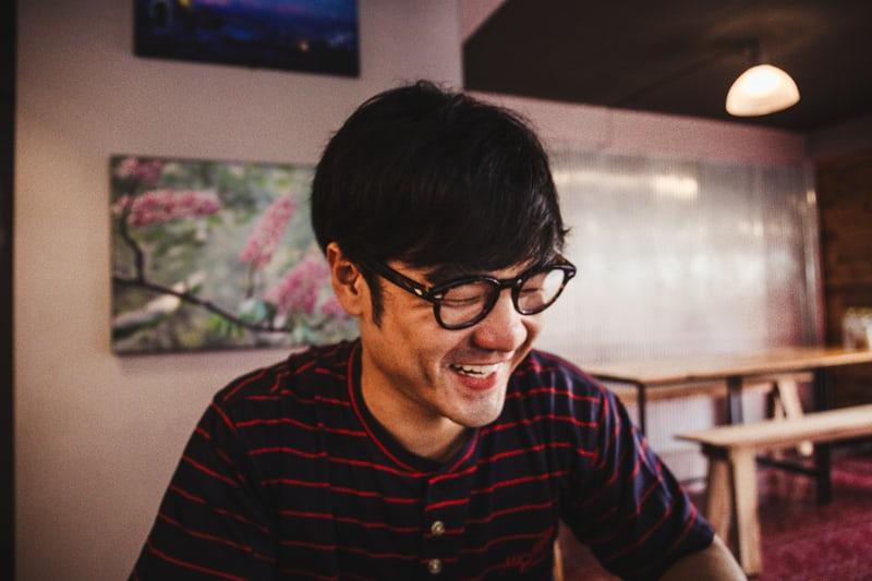 Ein koreanischer Mann mit schwarzer Brille blickt lachend zur Seite. In Düsseldorf gibt es viele koreanische Muttersprachler.