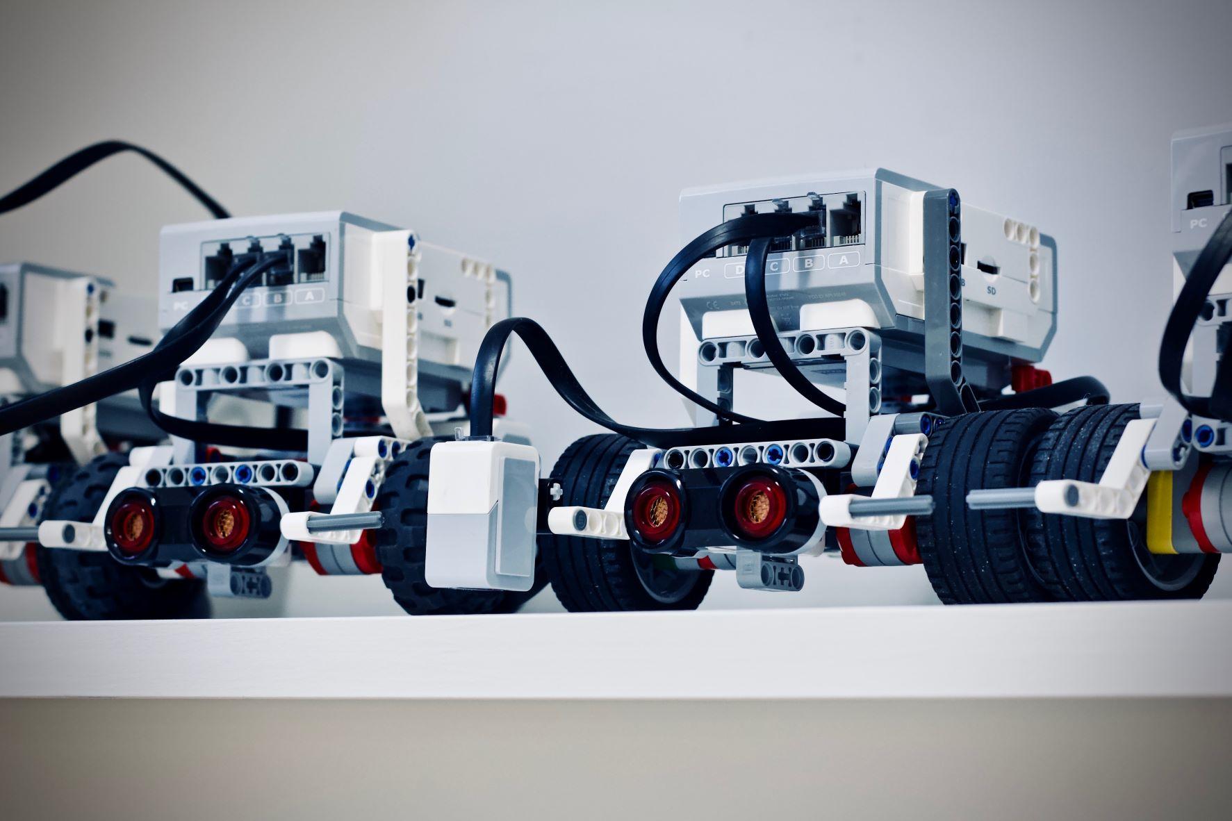 Zwei Roboter aus aus Lego, die einem Auto ähnlich sehen, stehen auf nebeneinander auf einem weißen Tisch. Egal ob aus Lego oder anderem Material, auf die Programmierung kommt es an.