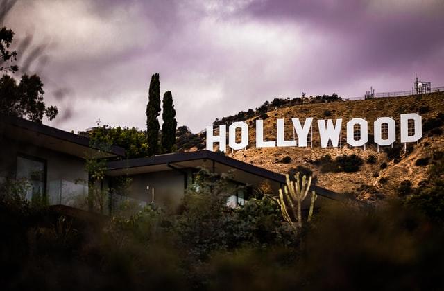 Das Hollywood Sign unter einem dramatischen Himmel mit einem Wohnhaus und Kakteen im Vordergrund. Einen Meisner Schauspielkurs kann man in LA und auch in Deutschland besuchen.