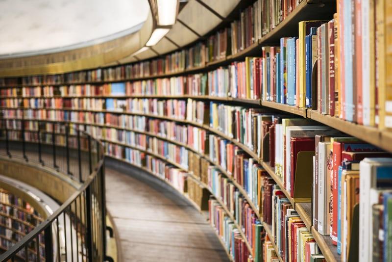 Ein Gang in einer Bibliothek mit Reihen bunter Buchrücken vom Boden bis zur Decke.