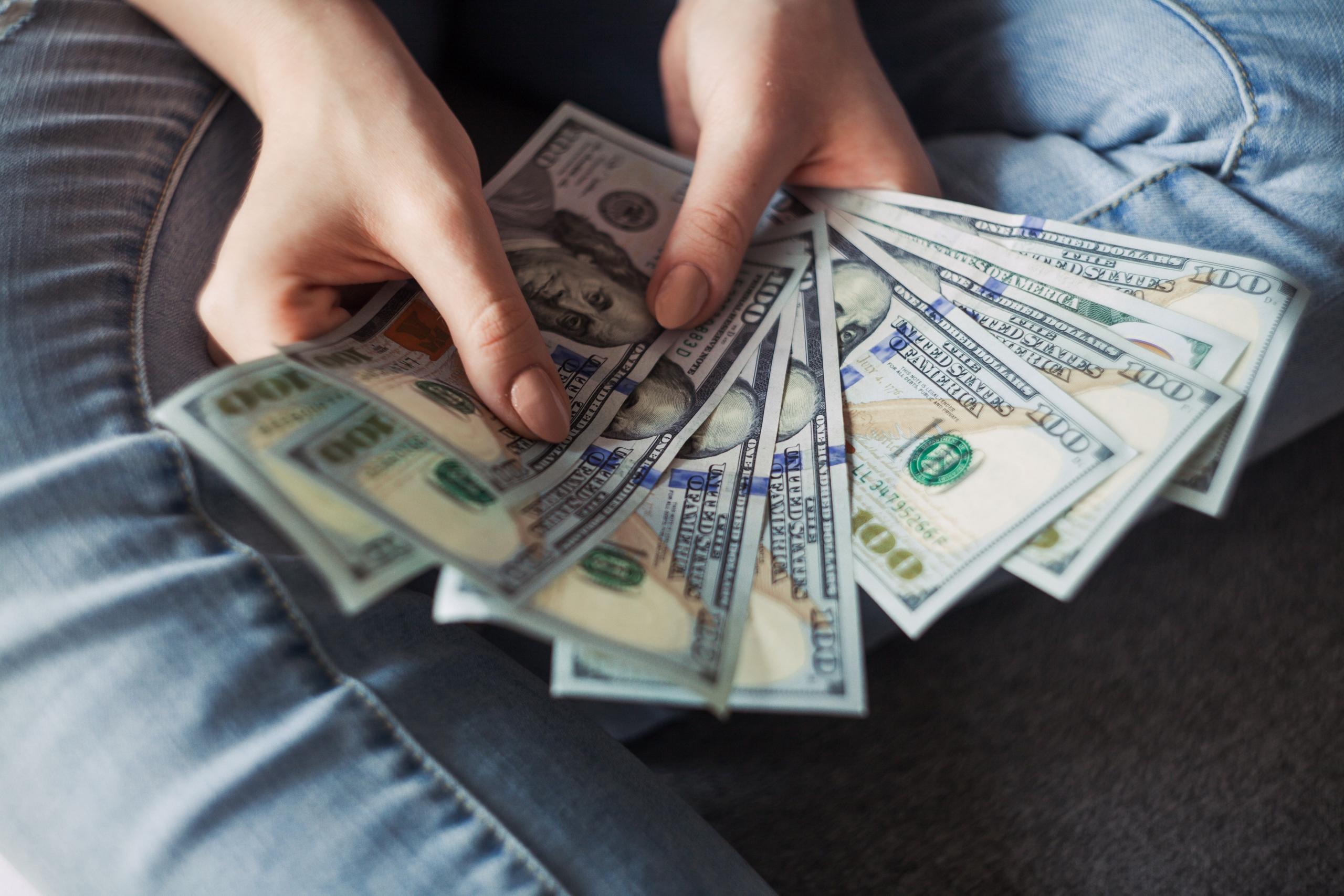 Frau hält amerikanische Dollar-Scheine als Fächer ausgebreitet in beiden Händen Hand.