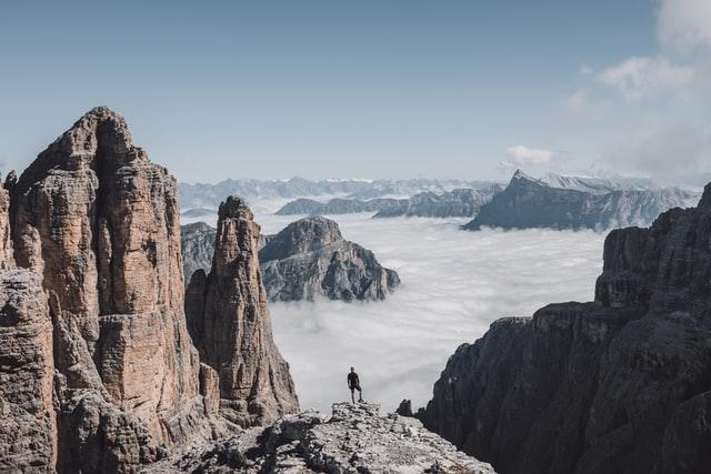 Ein Mann steht auf einem Felsvorsprung zwischen markanten Felsen und blickt auf das Nebelmeer über die Täler von Alto Adige!