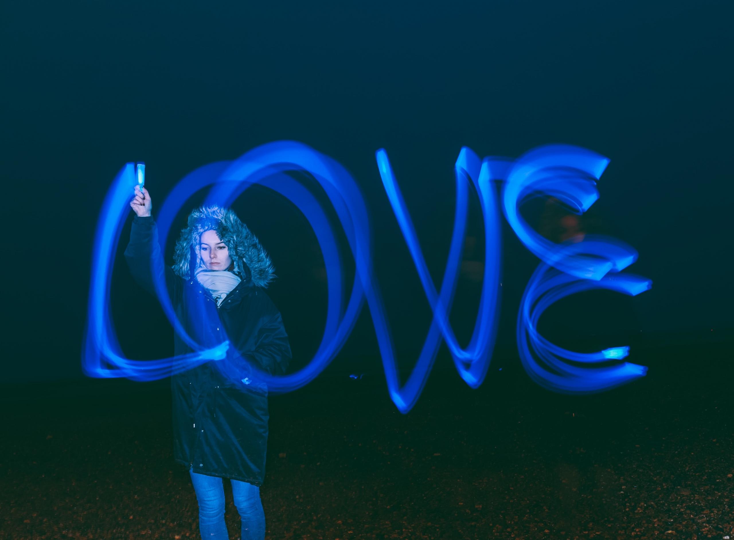 Eine Frau schreibt mit einem blauen Leuchtstab das Wort Love in die Luft.