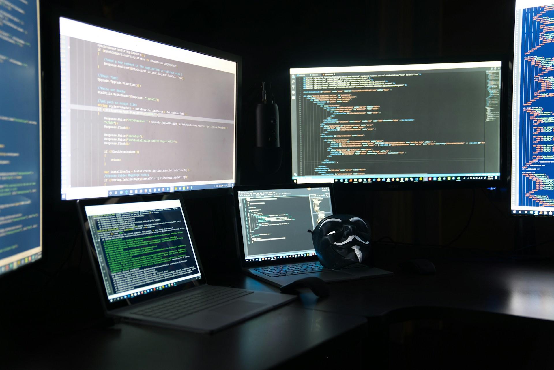 Auf mehreren Flachbildschirmen und Laptops steht ein Code in Programmiersprache