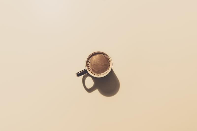 Auf einer beigefarbenen Tischplatte steht eine Keramiktasse mit Kaffee.
