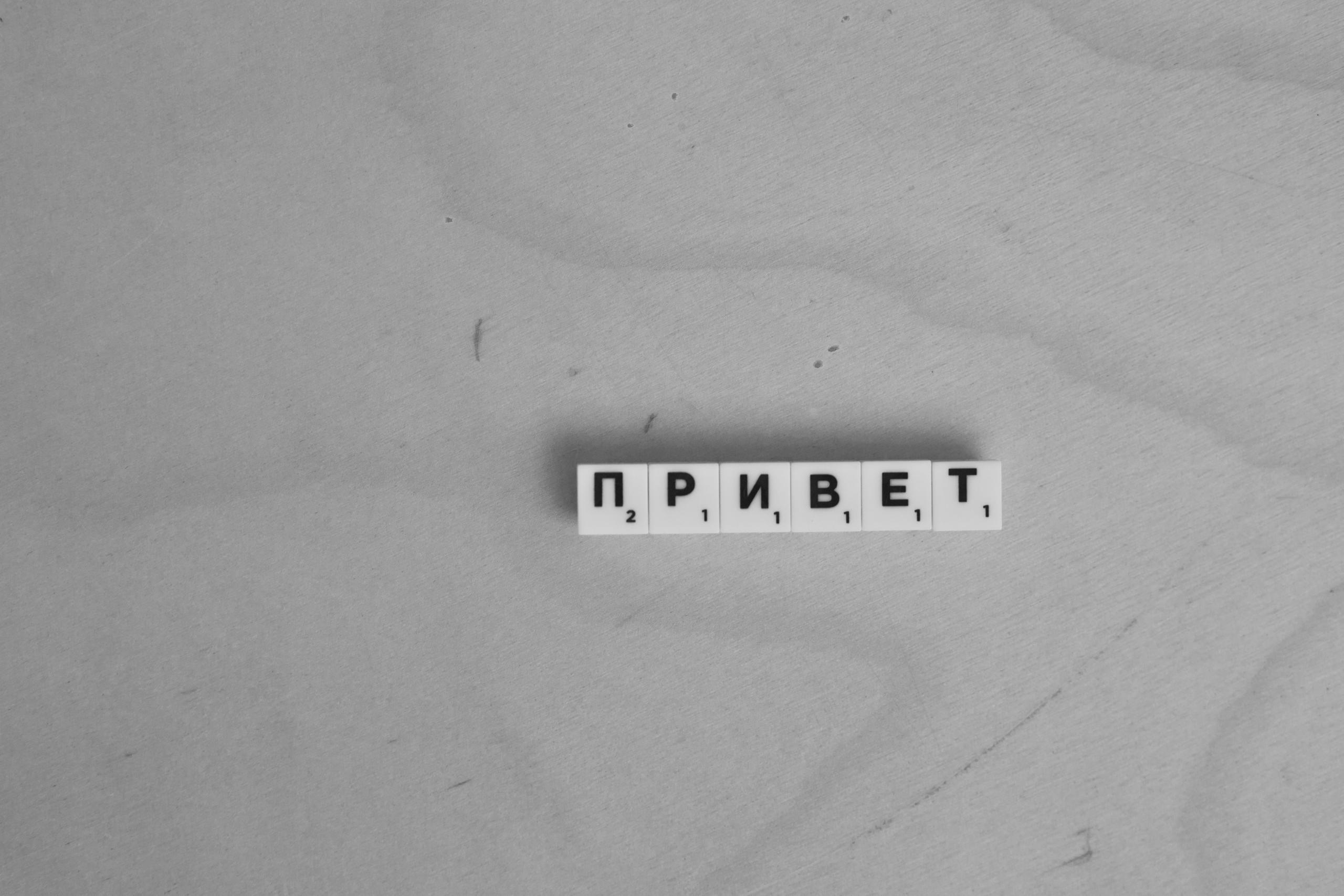 Auf einer Holzoberfläche steht mit Scrabble-Steine mit kyrillischen Buchstaben das Wort Privjet.