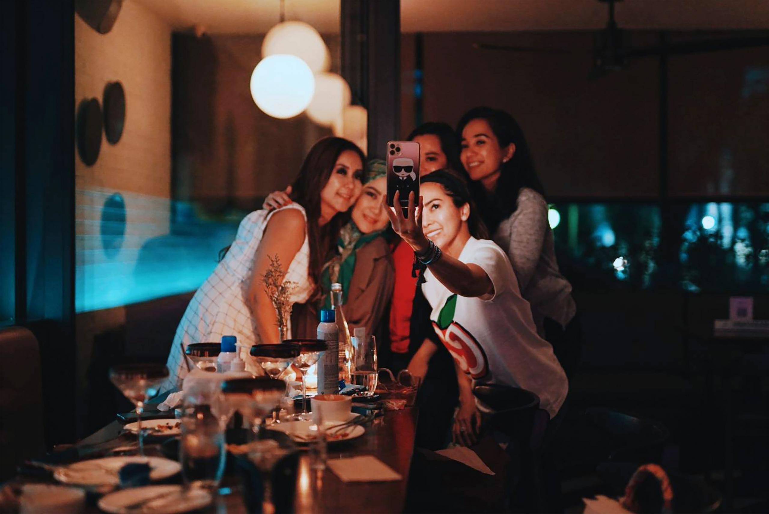 Fünf junge Frauen stehen in einer Bar dicht beisammen und machen lachend ein Selfie.