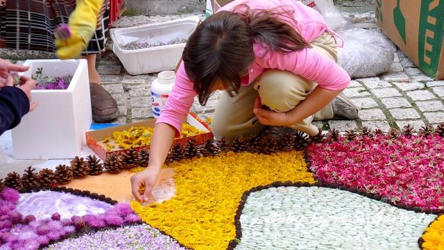 Eine Frau in der Hocke streut mit Blütenblättern ein Straßenbild für das Blumenfest!