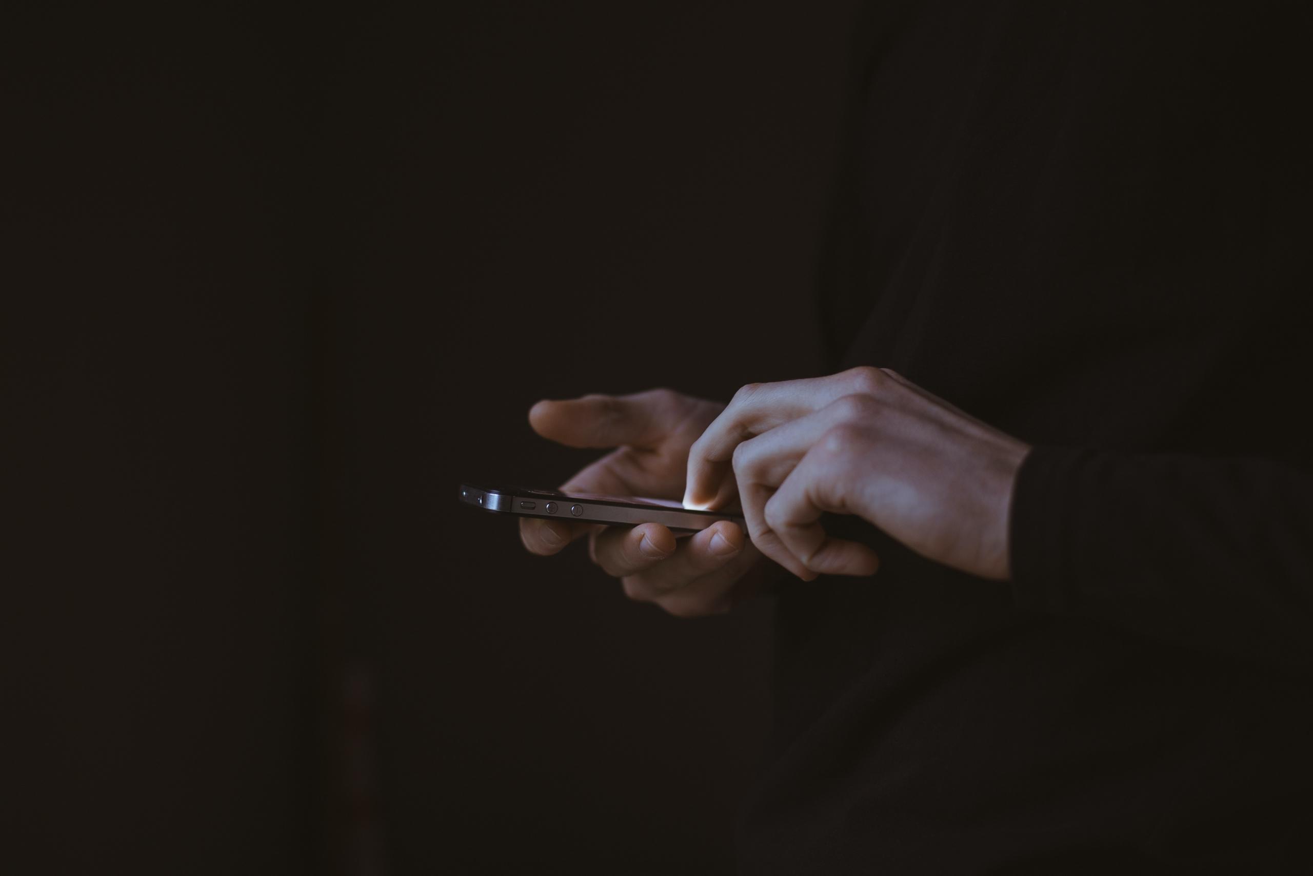 Jemand hält ein Smartphone in beiden Händen und streicht mit einem Finger über das Display.