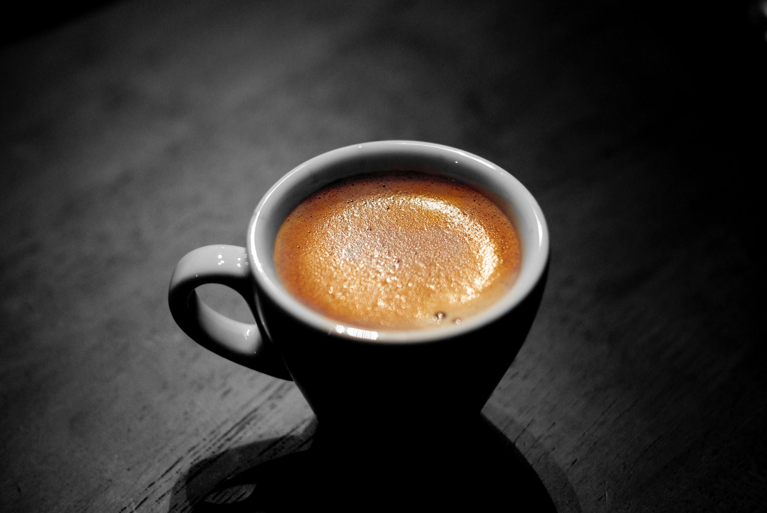 Ein volle Espresso-Tasse mit Schaumkrone steht auf einem schwarzen Tisch.