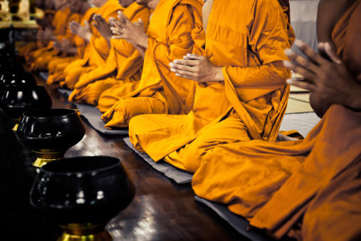 In einer Reihe sitzen betende buddhistische Mönche in safrangelben Gewändern. 